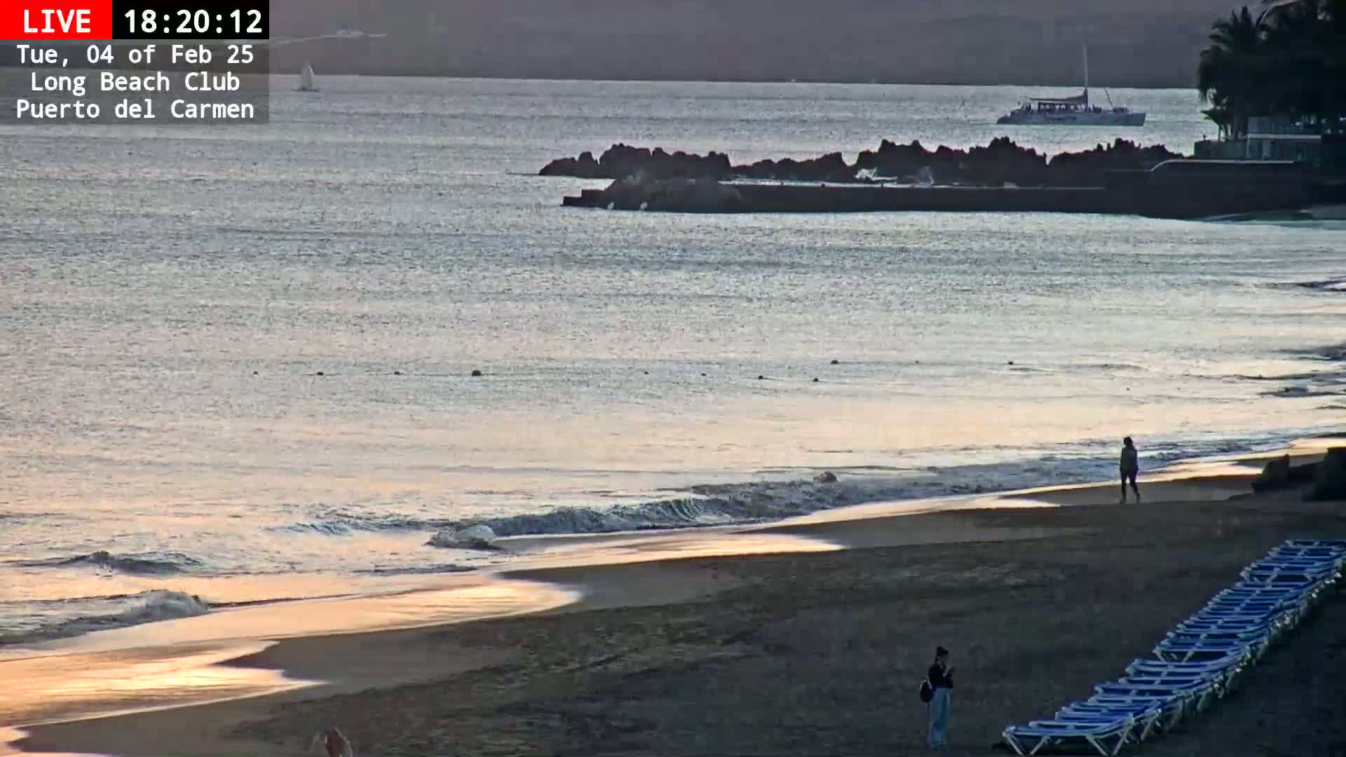 A sandy beach with calm waves and a few people is visible during what appears to be sunset or sunrise.