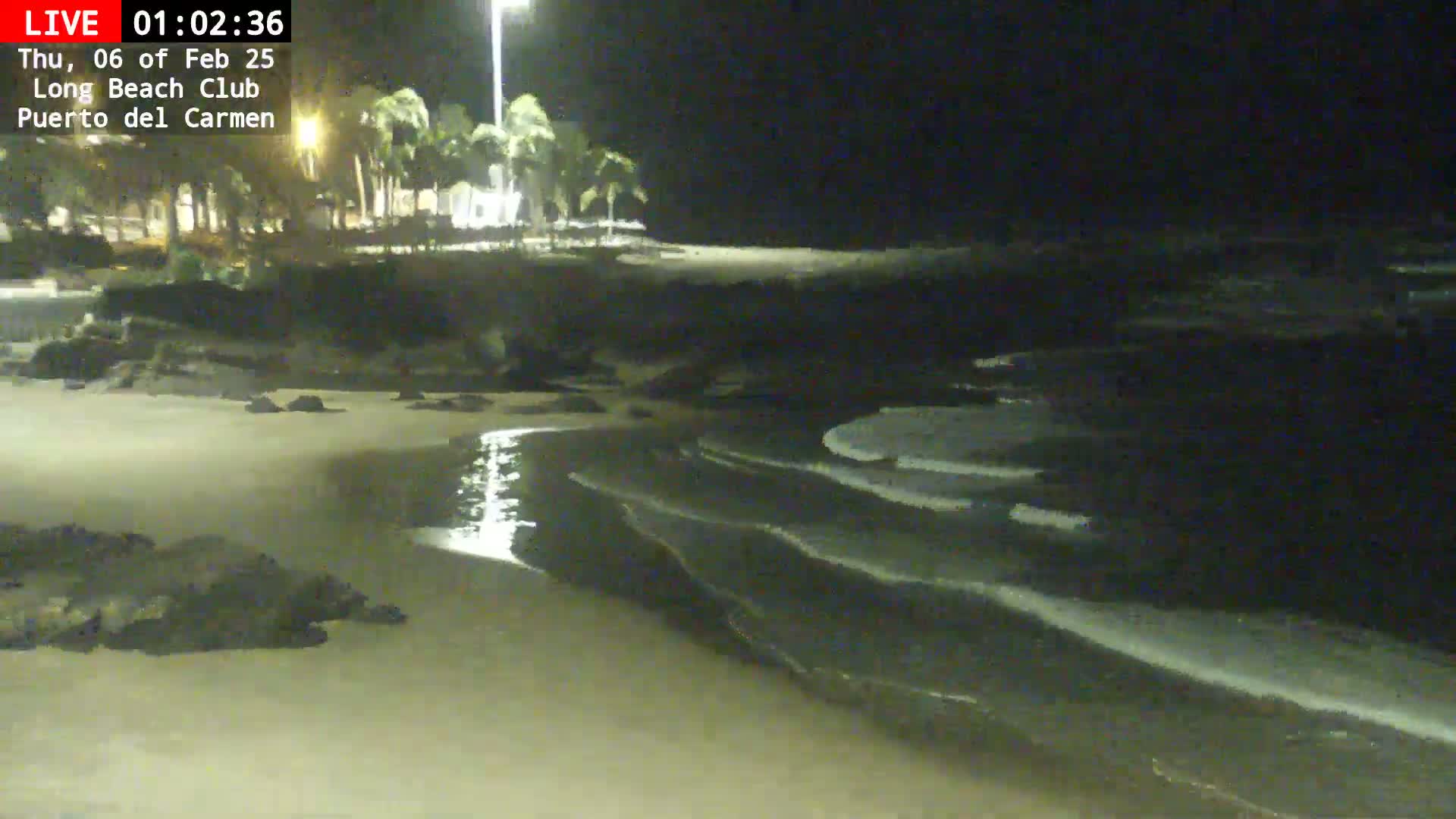 A sandy beach at night with gentle waves lapping the shore under a dark sky.
