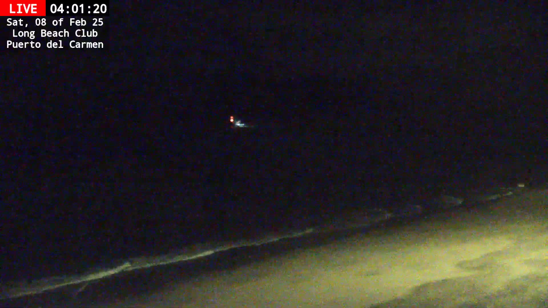 A dark, nighttime beach scene shows a gently lapping ocean and a distant light.