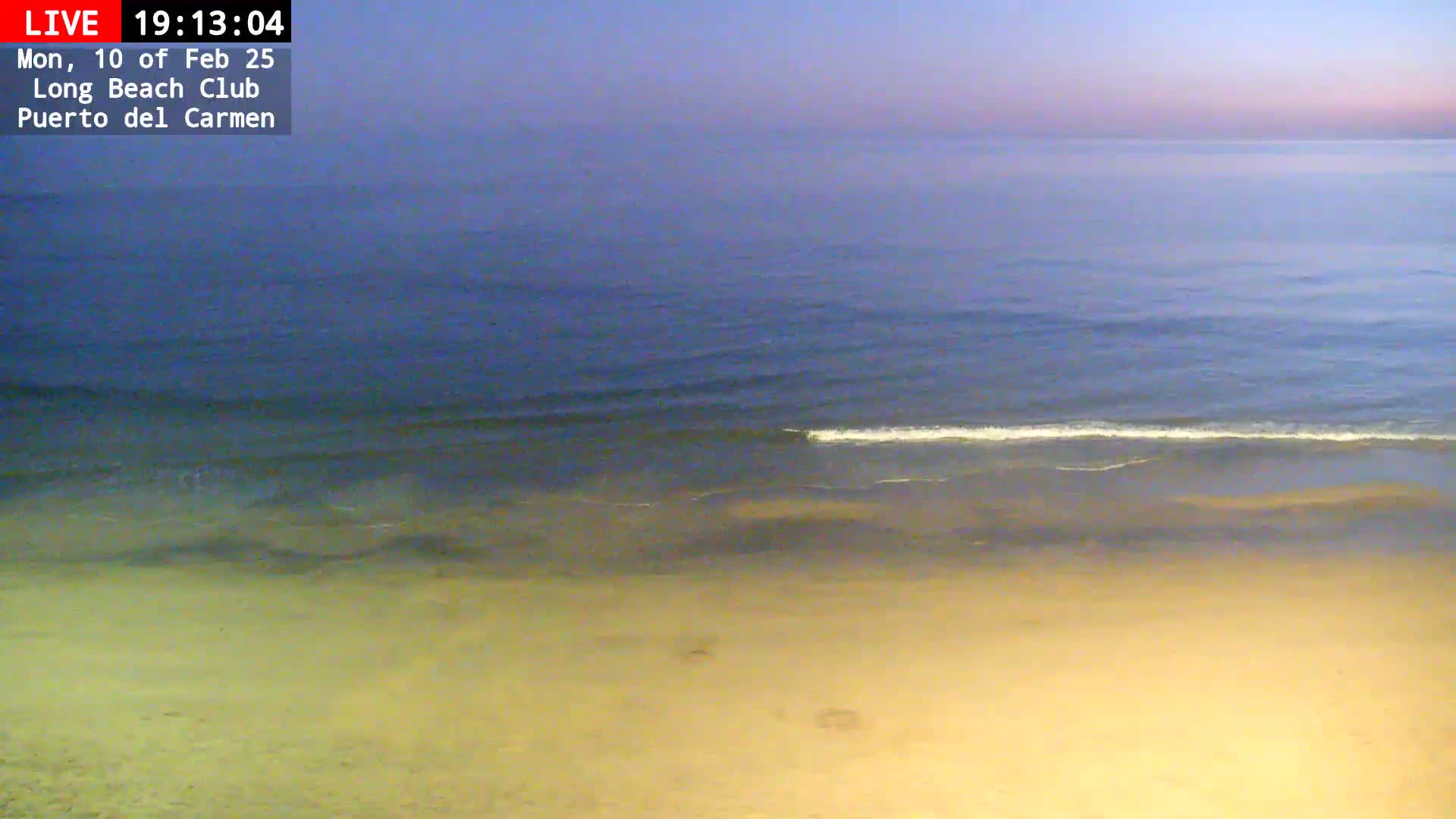 A sandy beach meets a calm, dark blue ocean under a twilight sky.