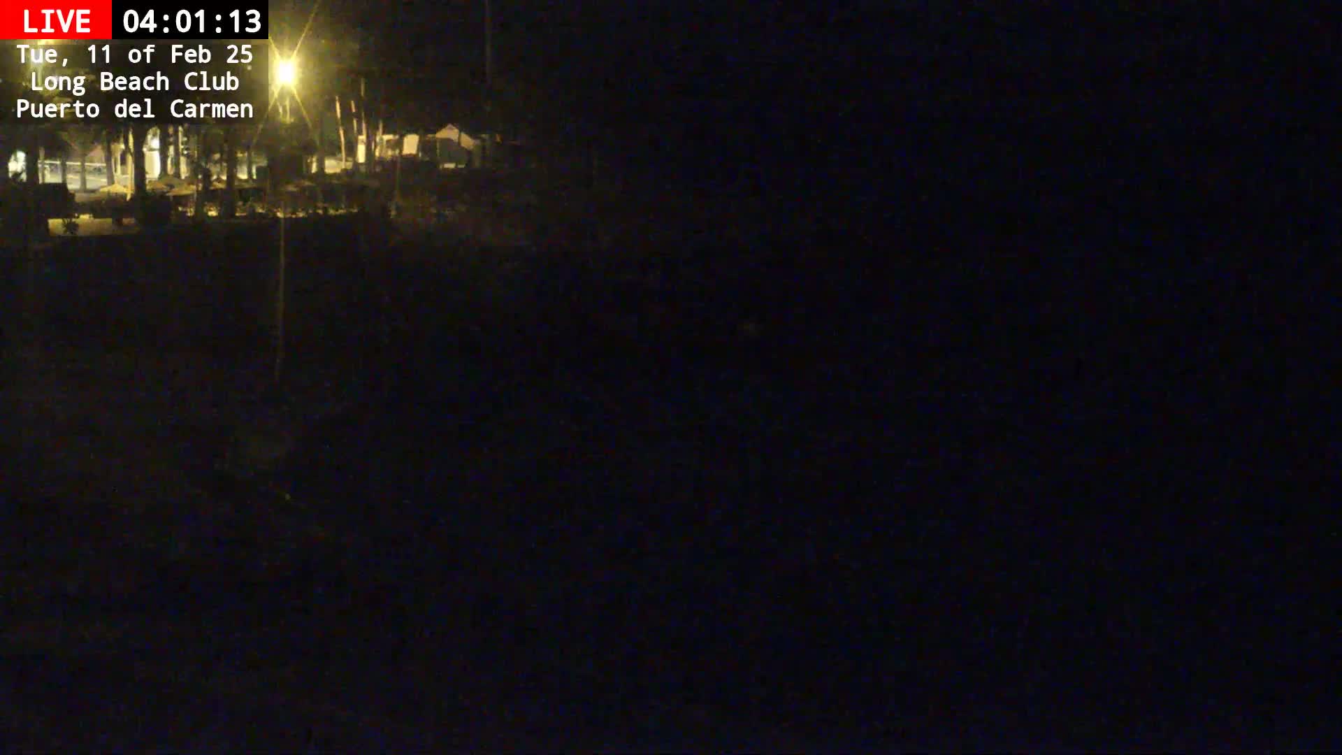 A dark, nighttime view of a dimly lit area, possibly a beach club, under a clear, dark sky.