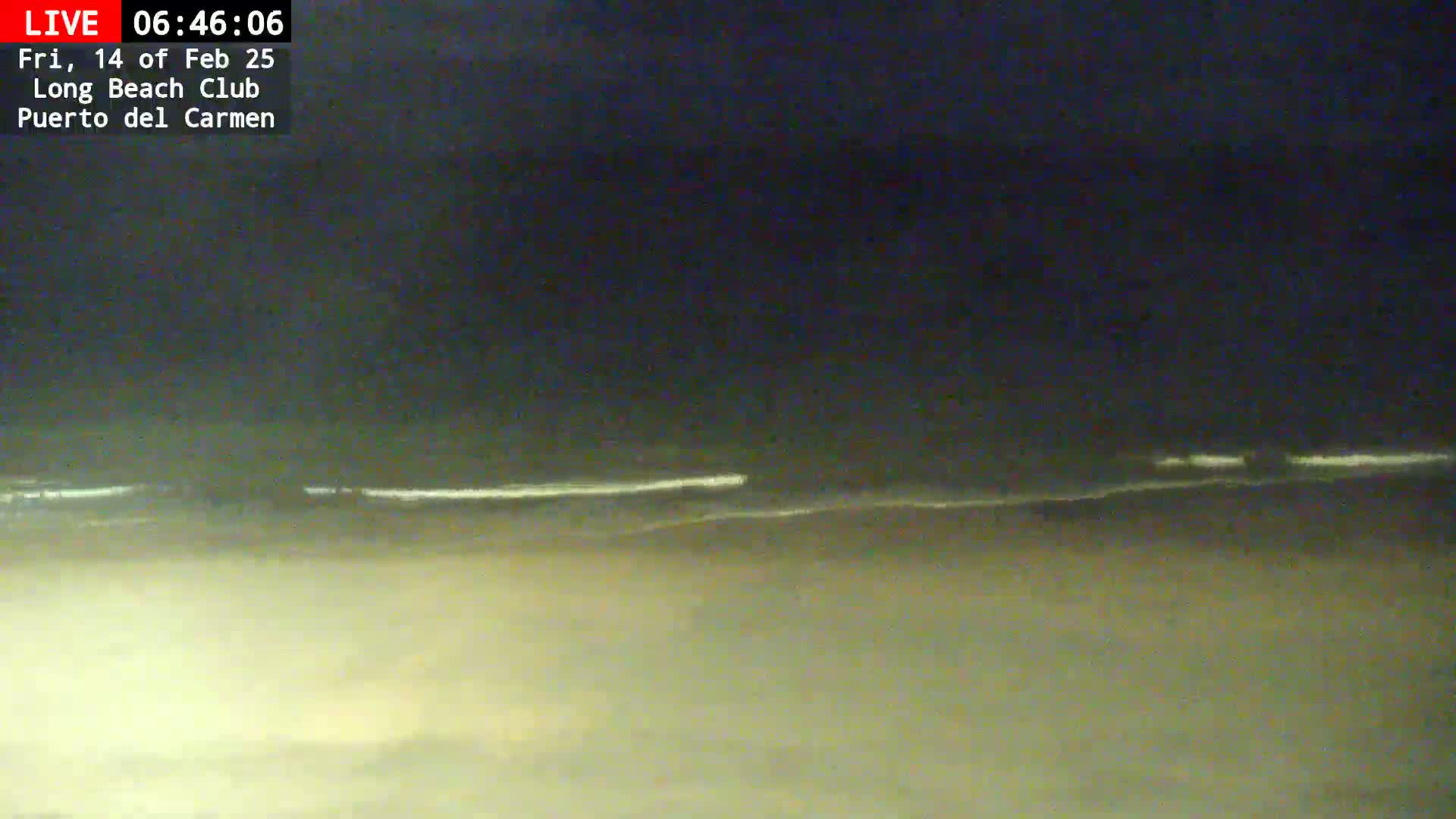 A nighttime beach scene shows a dark sky above a hazy, light-colored beach and dark ocean with faintly visible waves.