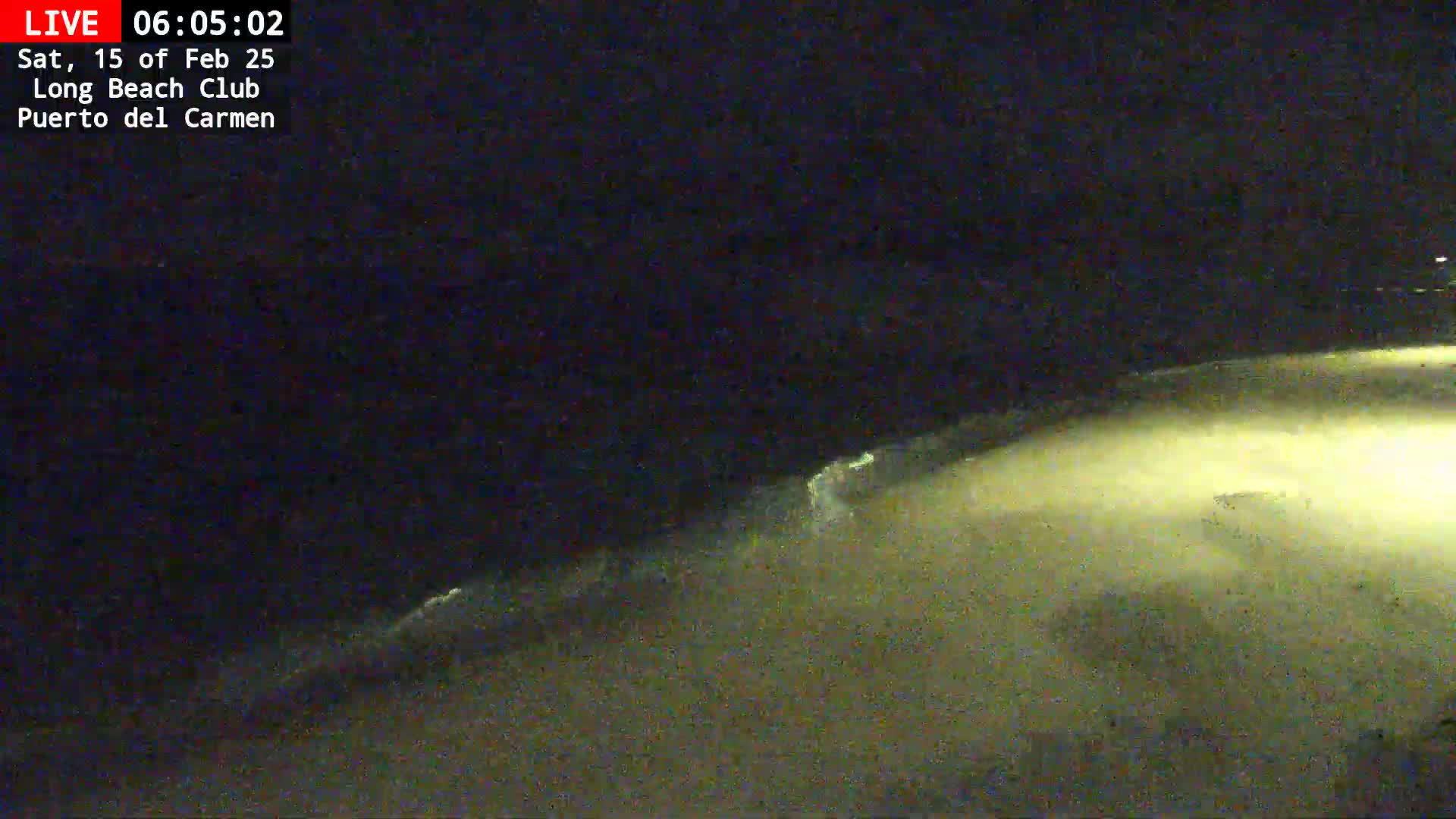 A dark, nighttime beach scene shows dimly lit sand and small waves lapping the shore.