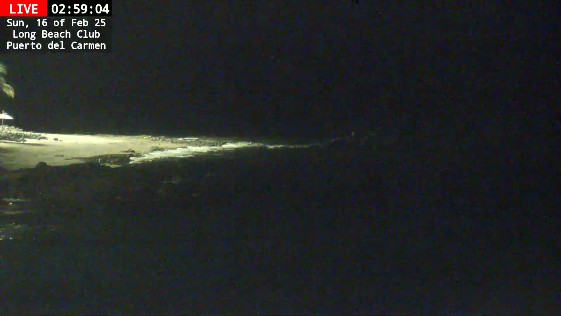A dark, nighttime beach scene shows a dimly lit shoreline with a small amount of wave action.