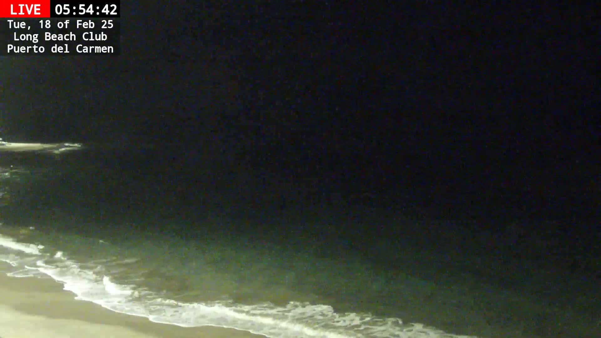 A nighttime beach scene shows gently lapping waves on a sandy shore under a dark sky.