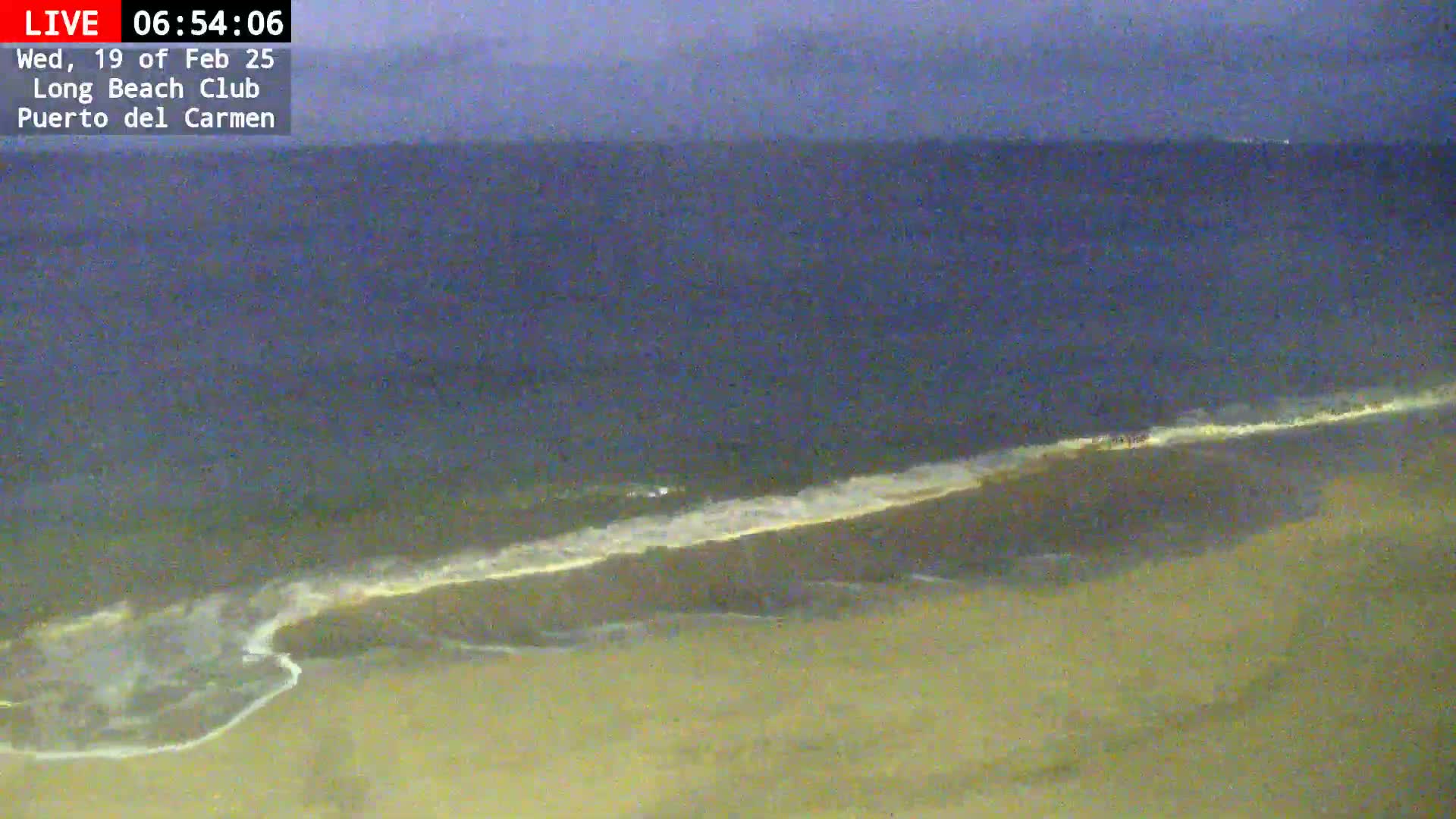 A sandy beach meets a dark-blue ocean under a dusky sky, with small waves lapping the shore.