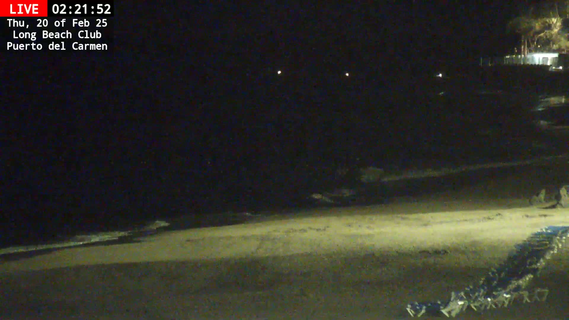 A dark, nighttime beach scene shows gently lapping waves on a sandy shore with beach chairs lined up in the lower right corner.