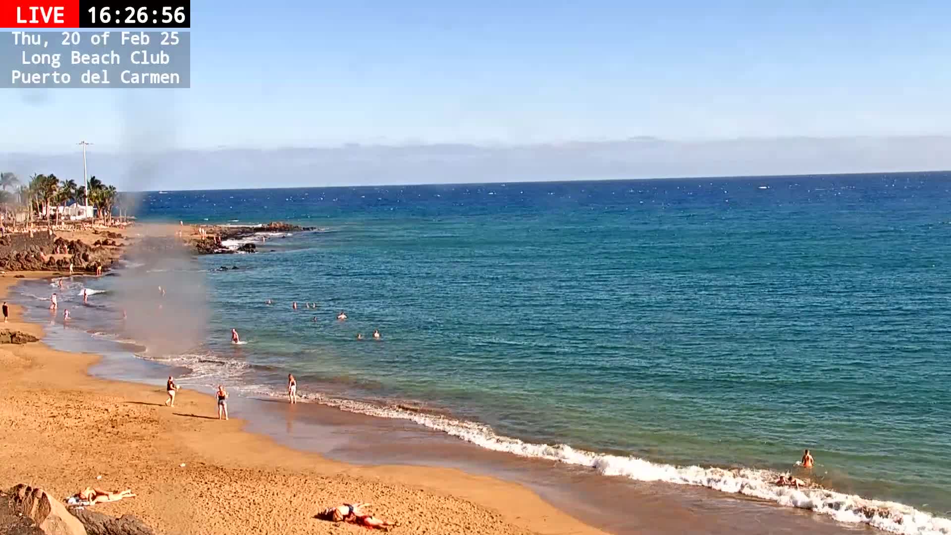 A sandy beach with people swimming and sunbathing, under a clear blue sky, next to a calm, turquoise ocean.