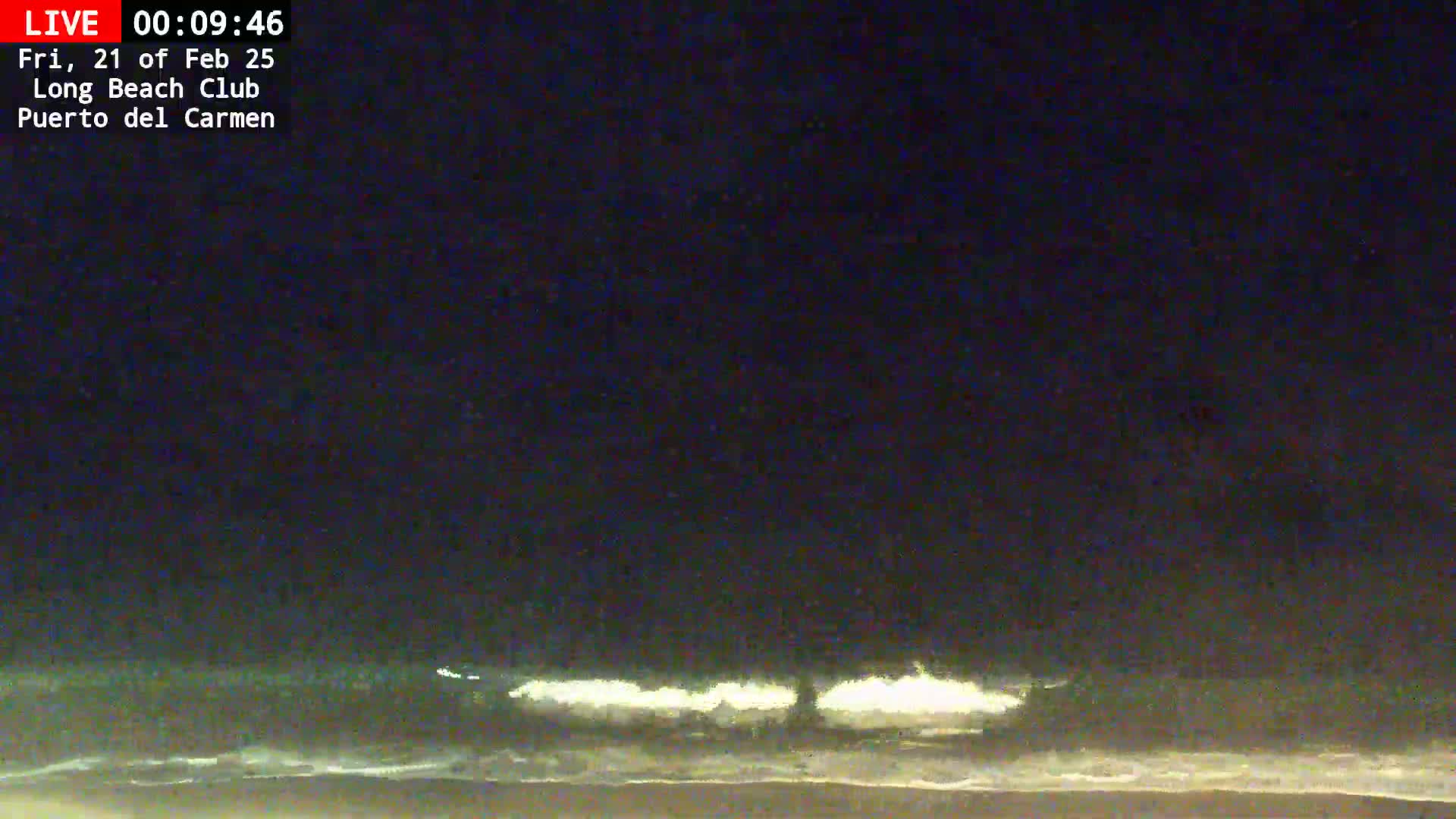 Under a dark night sky, small waves lap a sandy beach.