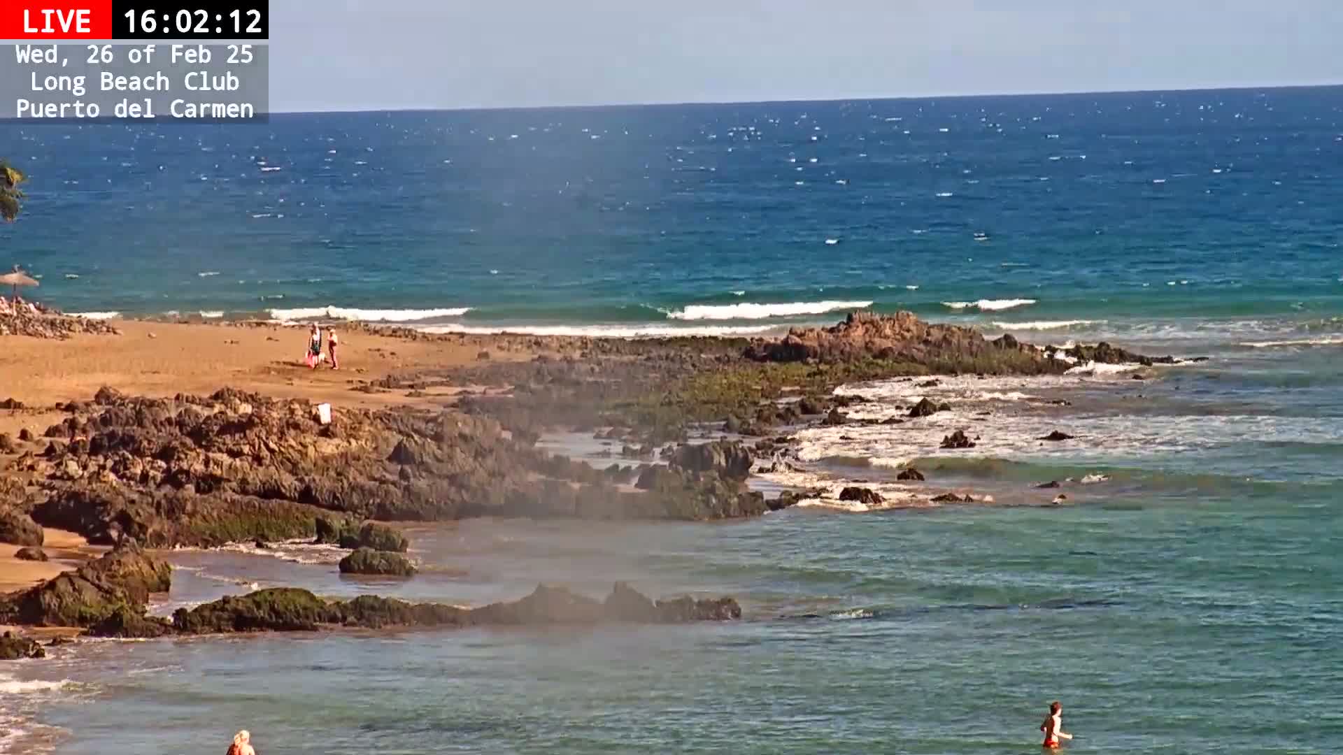 A sandy beach with dark rocks and small waves on a sunny day.