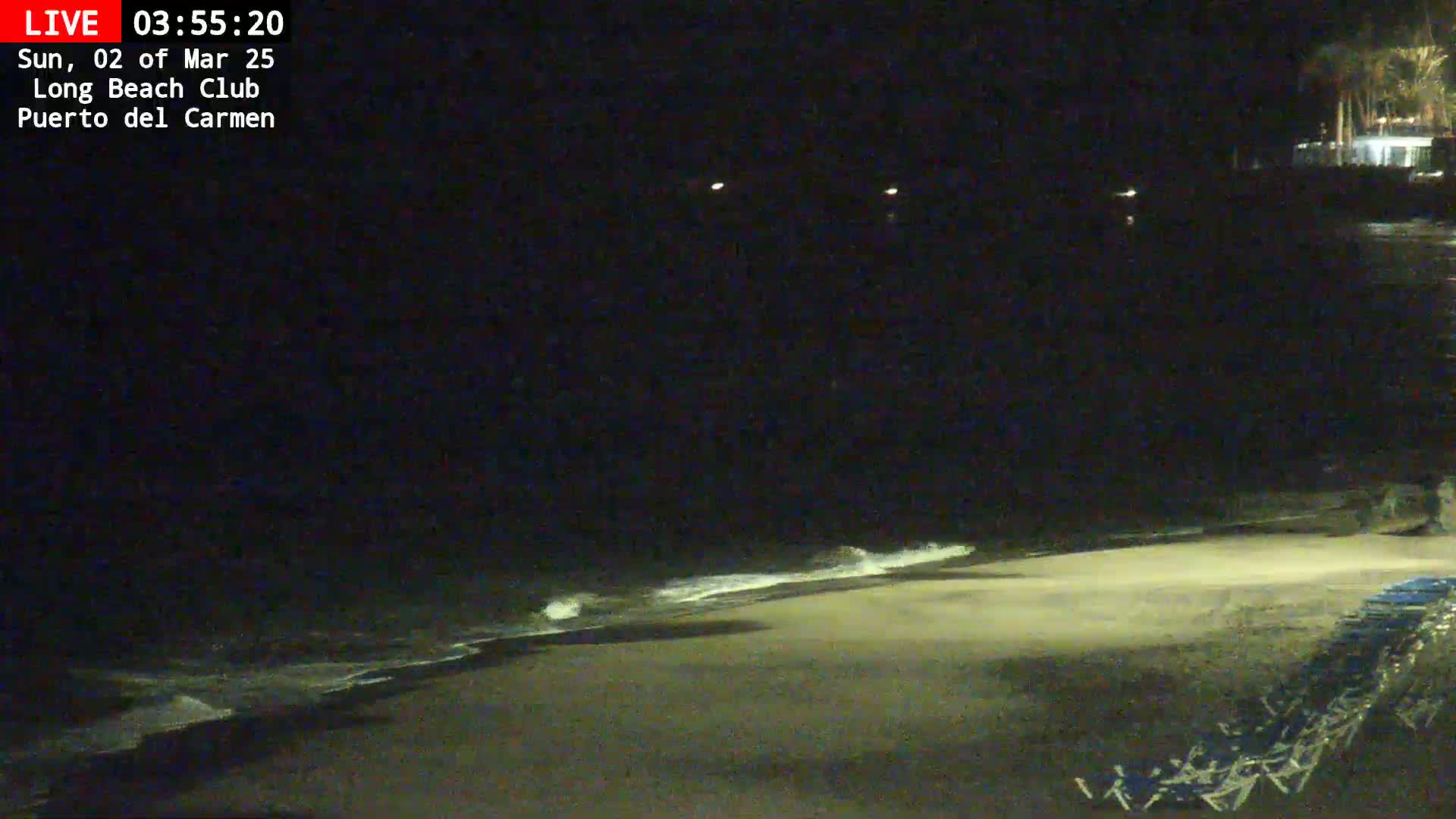 A dark, nighttime beach scene shows gently lapping waves on a sandy shore with beach chairs in the bottom right corner.