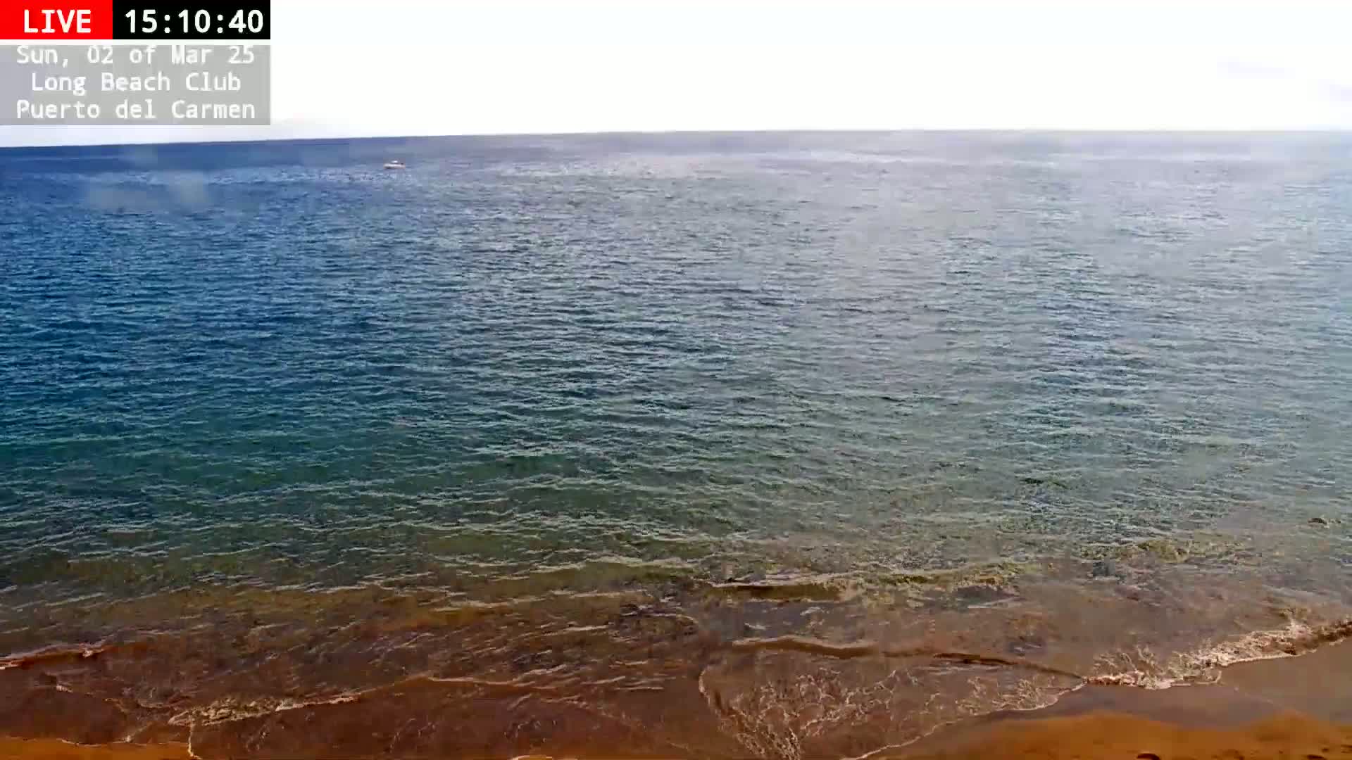 A mostly calm ocean with small waves lapping a sandy shore under a bright, clear sky.