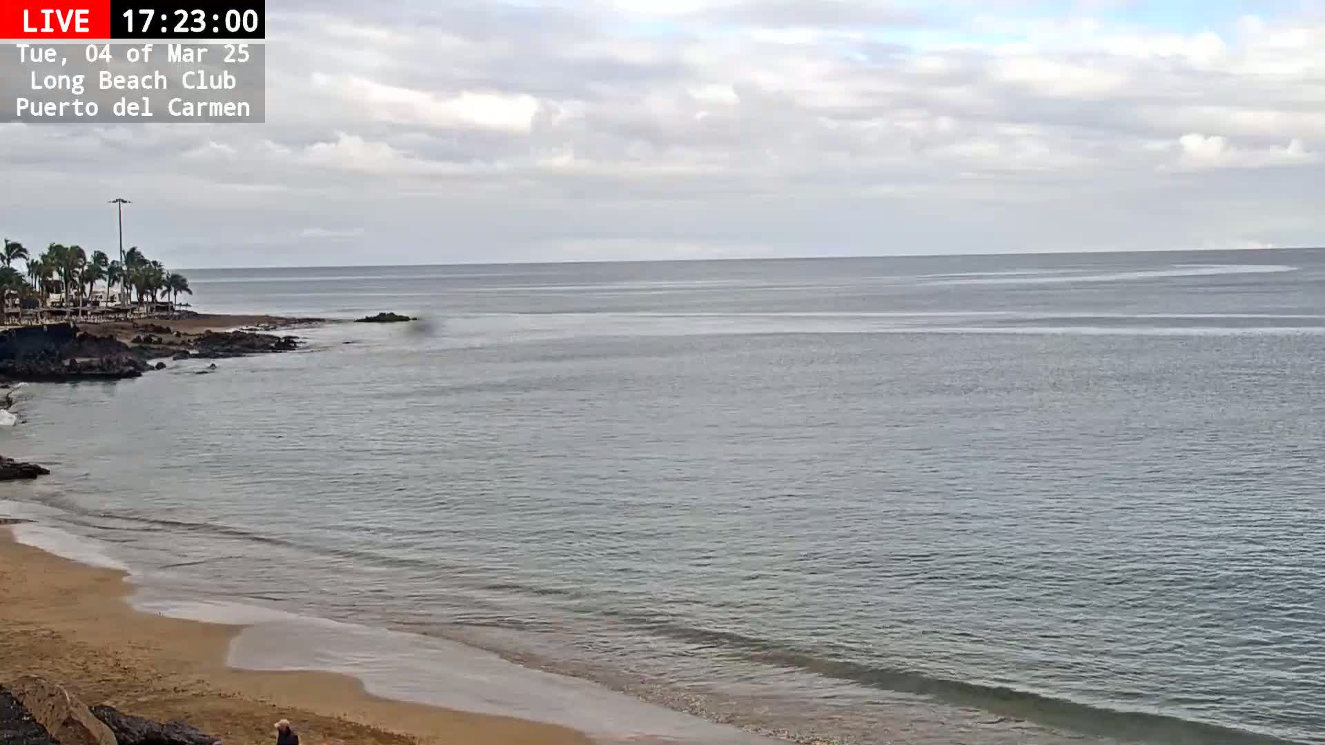 A sandy beach with calm, grey-green water under a partly cloudy sky.