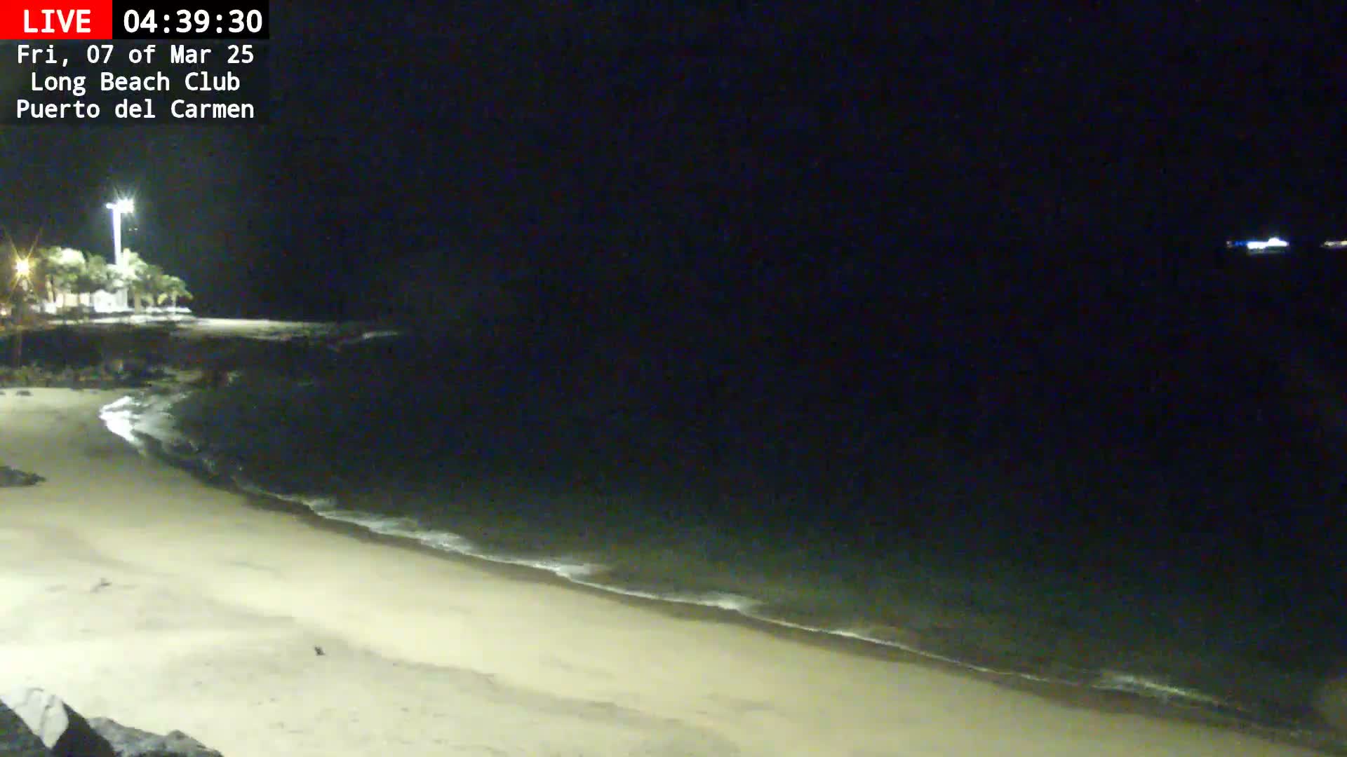 A sandy beach at night with gentle waves lapping the shore under a dark sky.