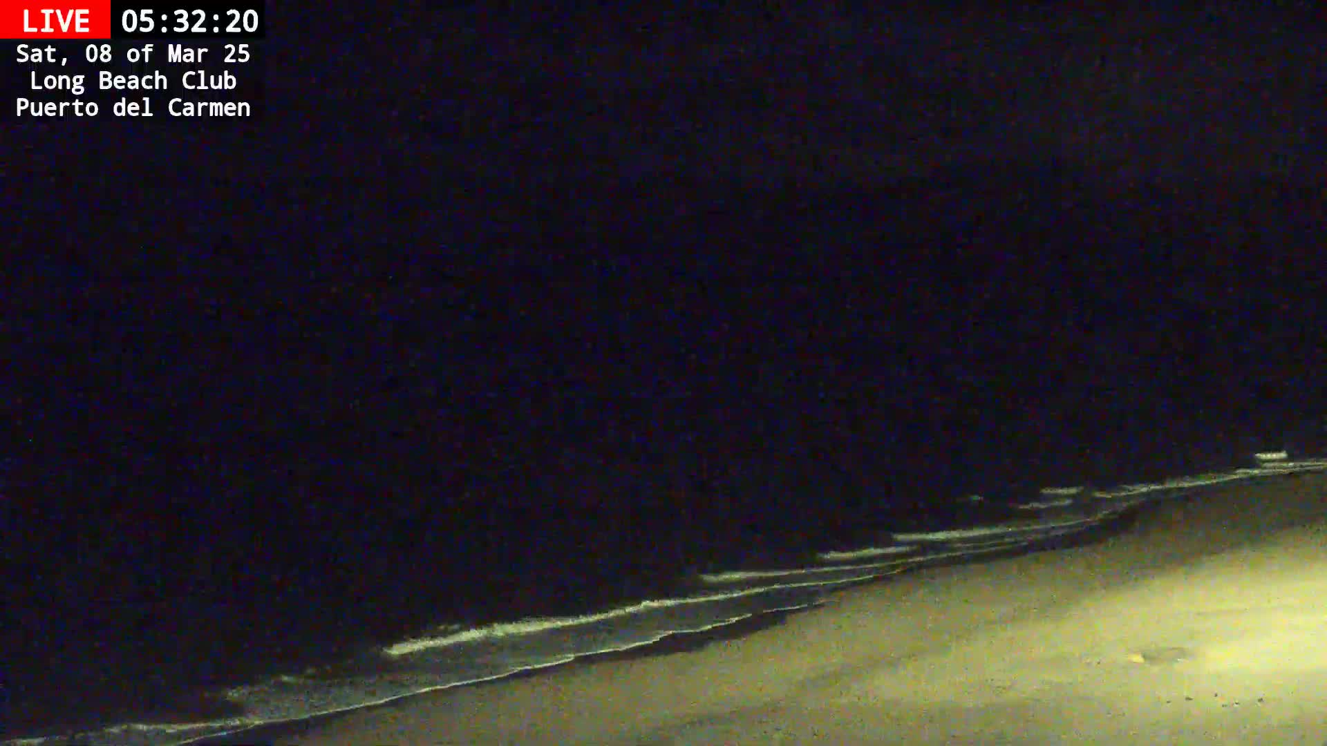 A dark, nighttime beach scene shows gentle waves lapping at the shore under a clear, black sky.