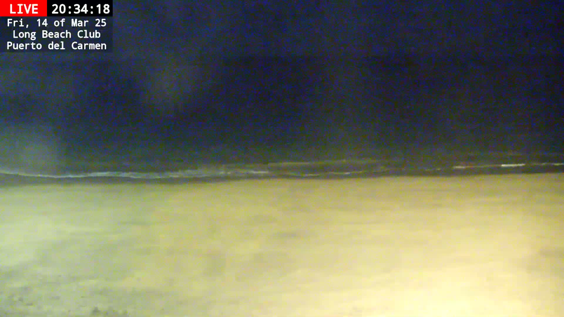 A dark nighttime beach scene shows a gently lapping ocean under a mostly clear sky.