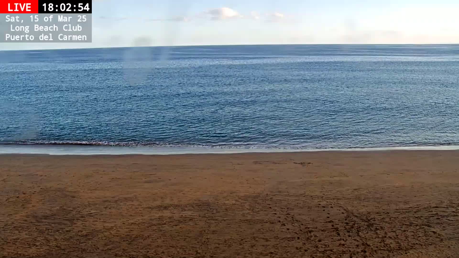 A sandy beach meets a calm, blue ocean under a clear sky.
