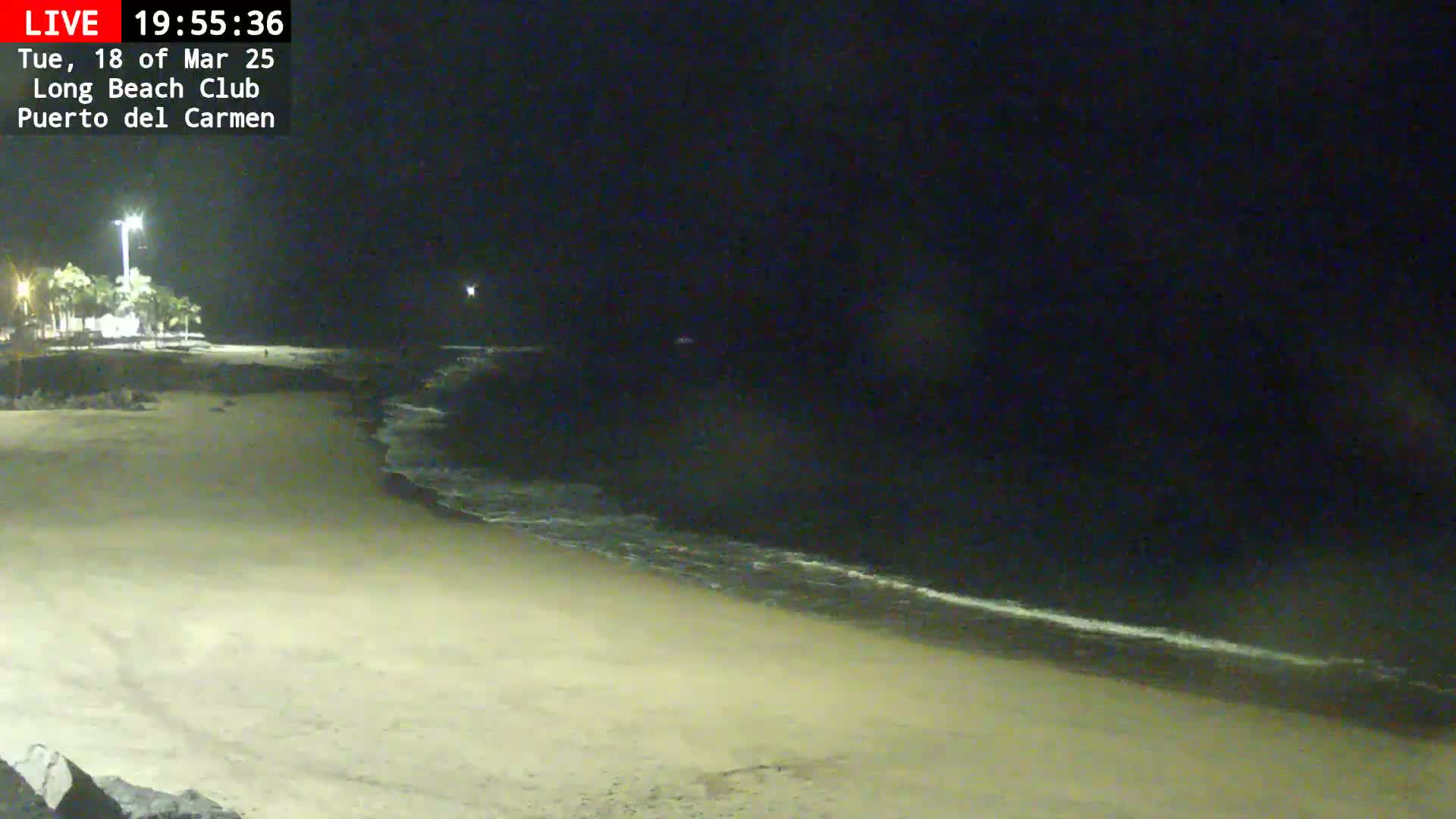 A dark, sandy beach at night with gently lapping waves under a clear sky.