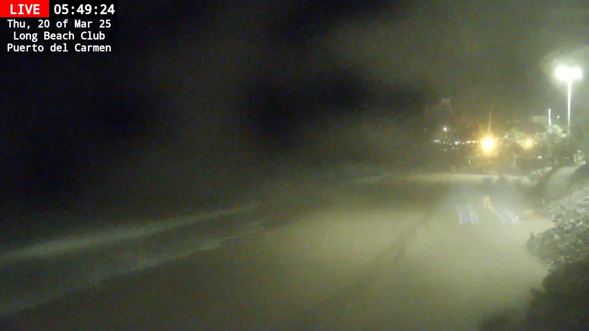 A nighttime, blurry view of a flooded area near a shoreline, illuminated by a streetlight.