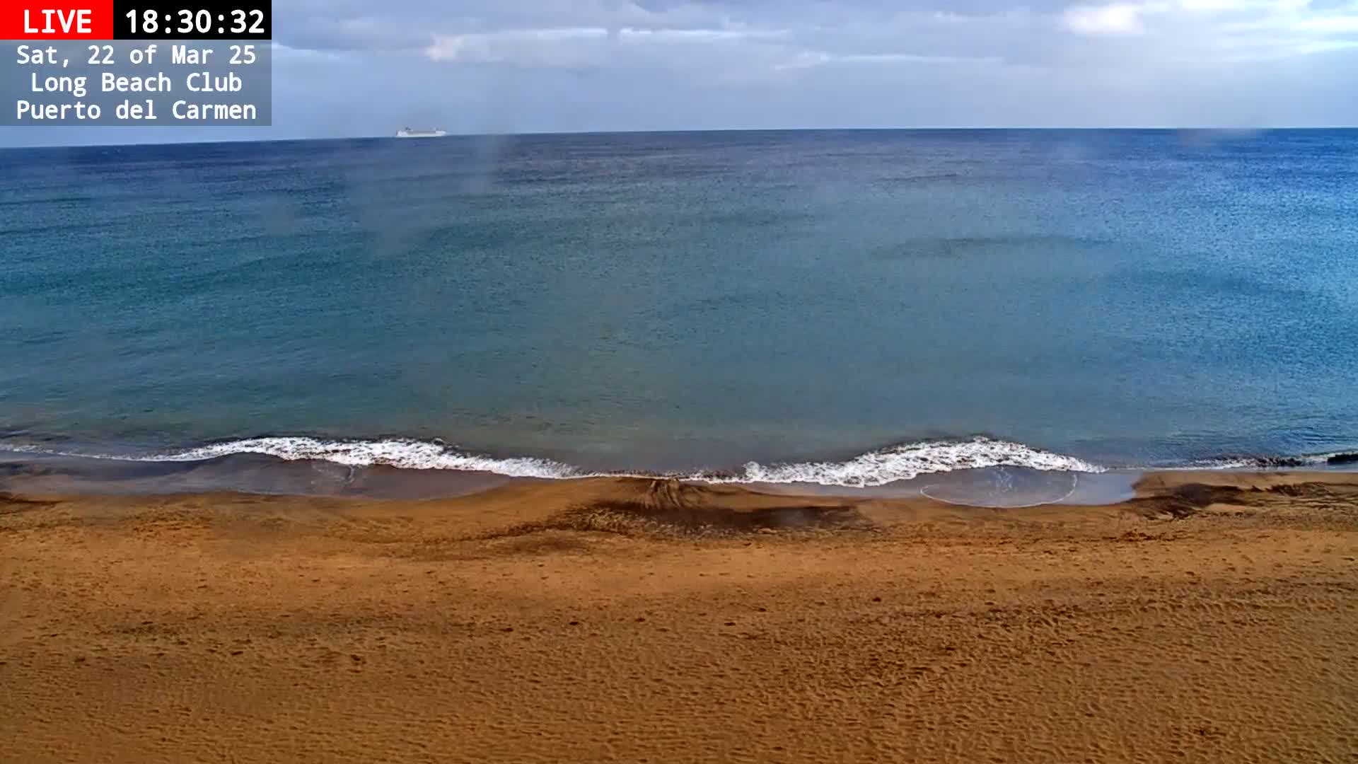 A sandy beach meets a calm, blue ocean under an overcast sky.