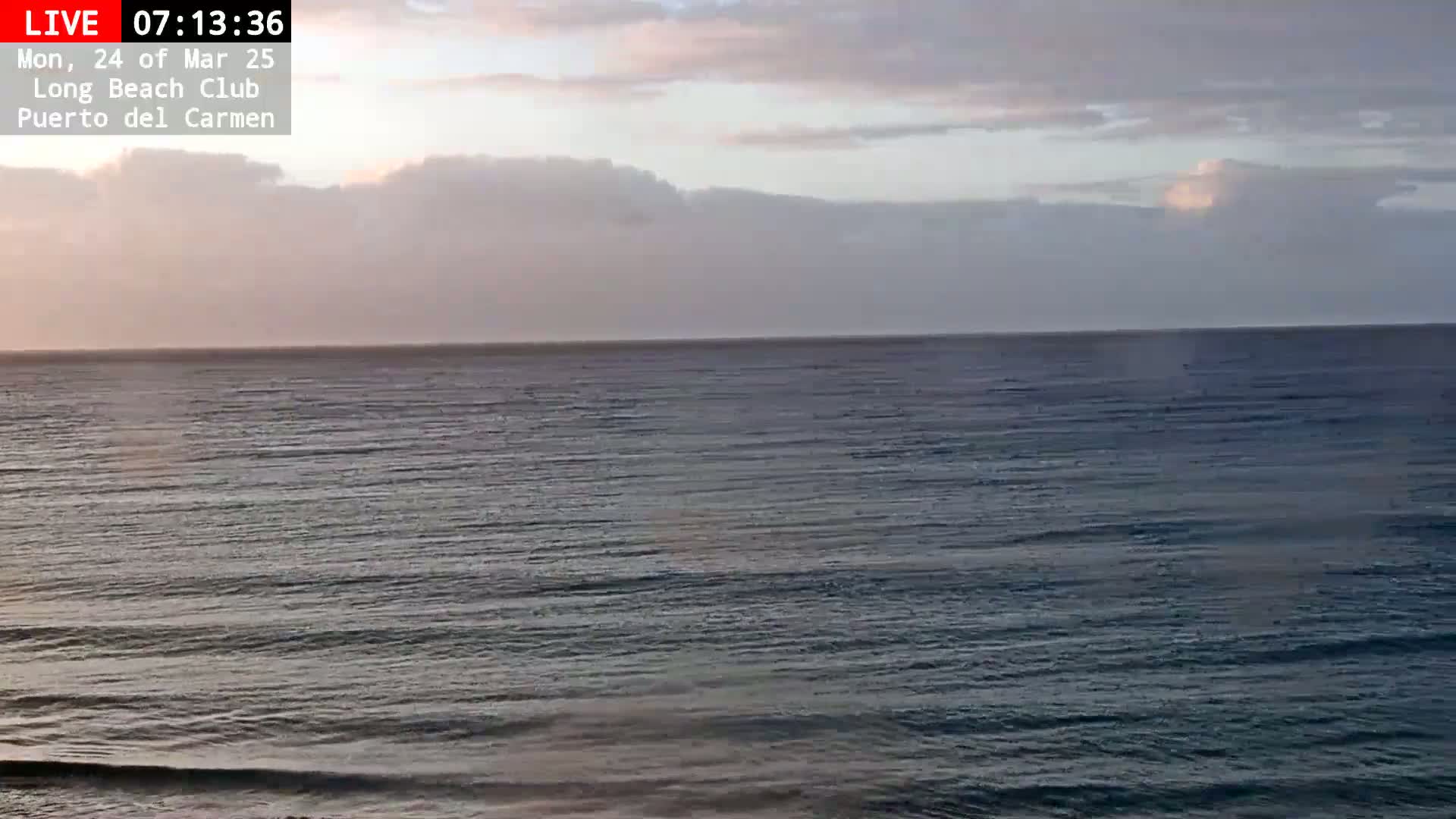 A calm ocean under a mostly cloudy, pale sky at sunrise.