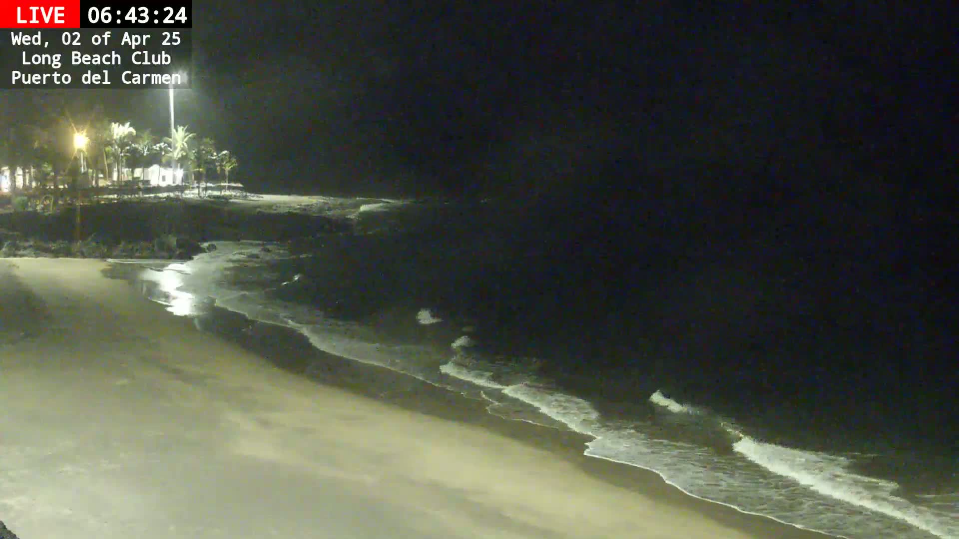 A sandy beach at night with gently lapping waves under a dark sky.