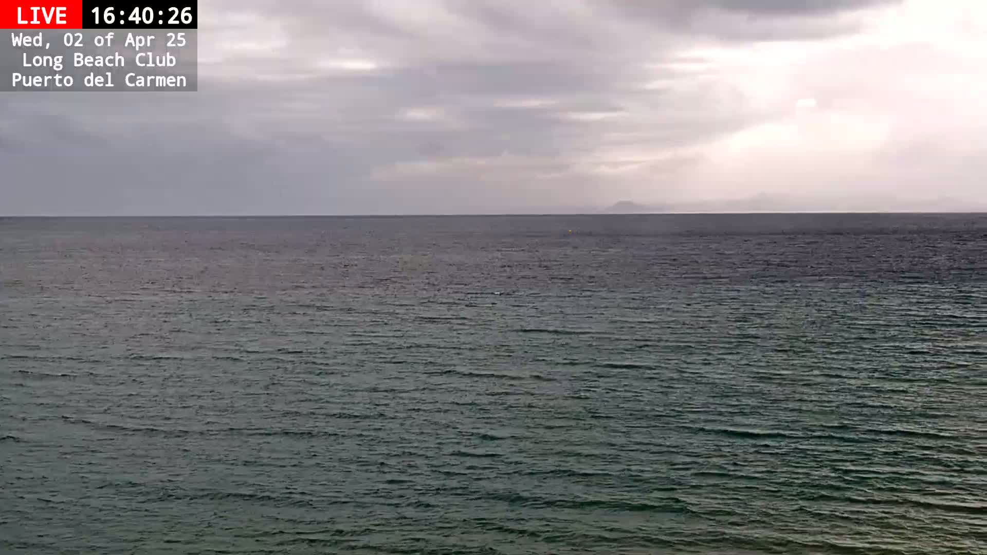 A calm, dark-green ocean stretches to a distant coastline under a cloudy sky.