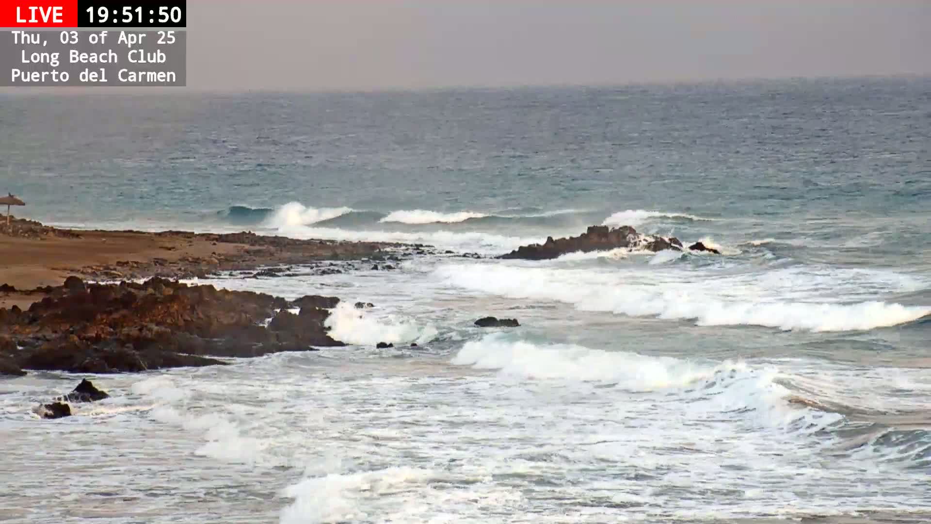Waves crash against a rocky shoreline on an overcast day.