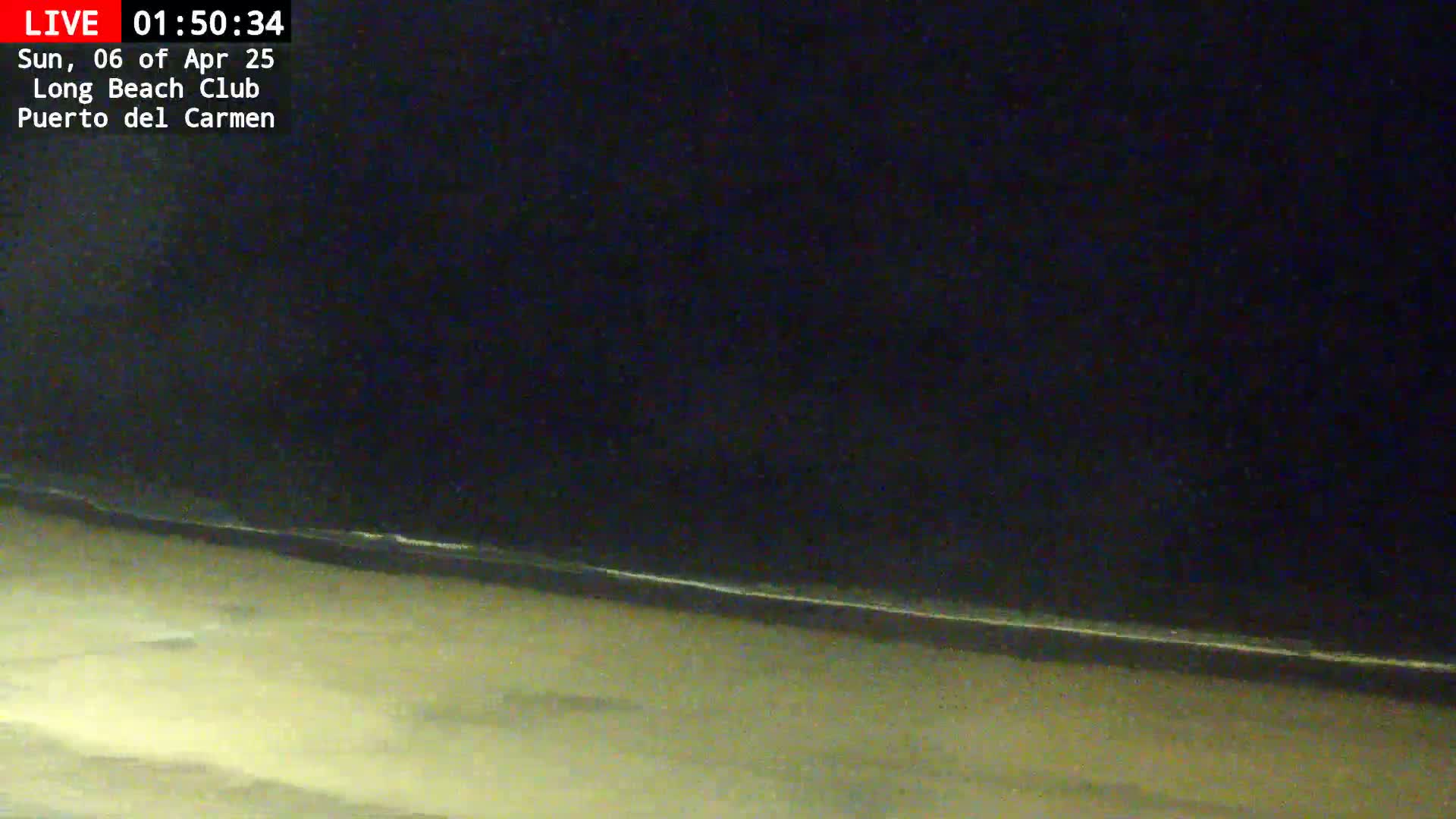 A dark beach at night with gently lapping waves under a clear, starless sky.