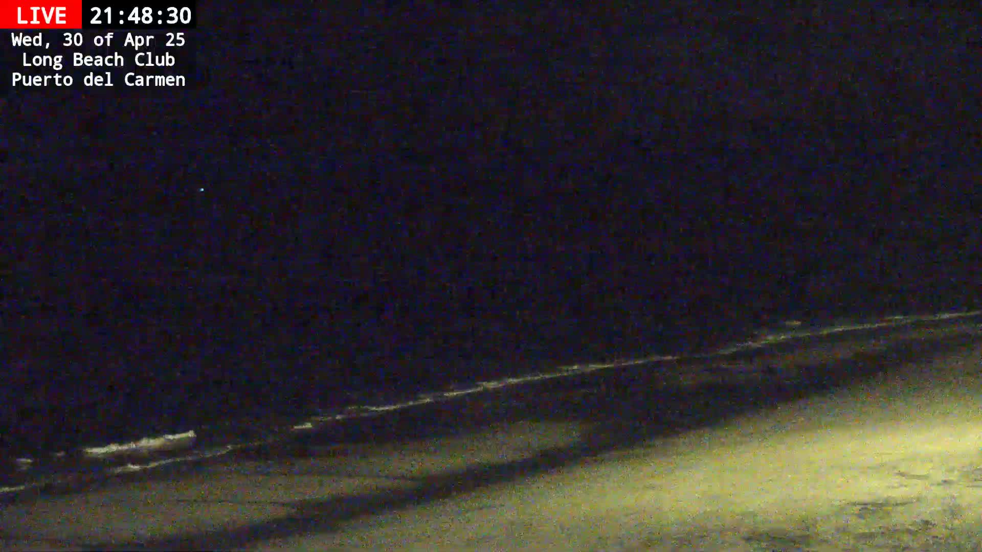 A dark, nighttime beach scene shows gentle waves lapping at the shore under a clear, starlit sky.