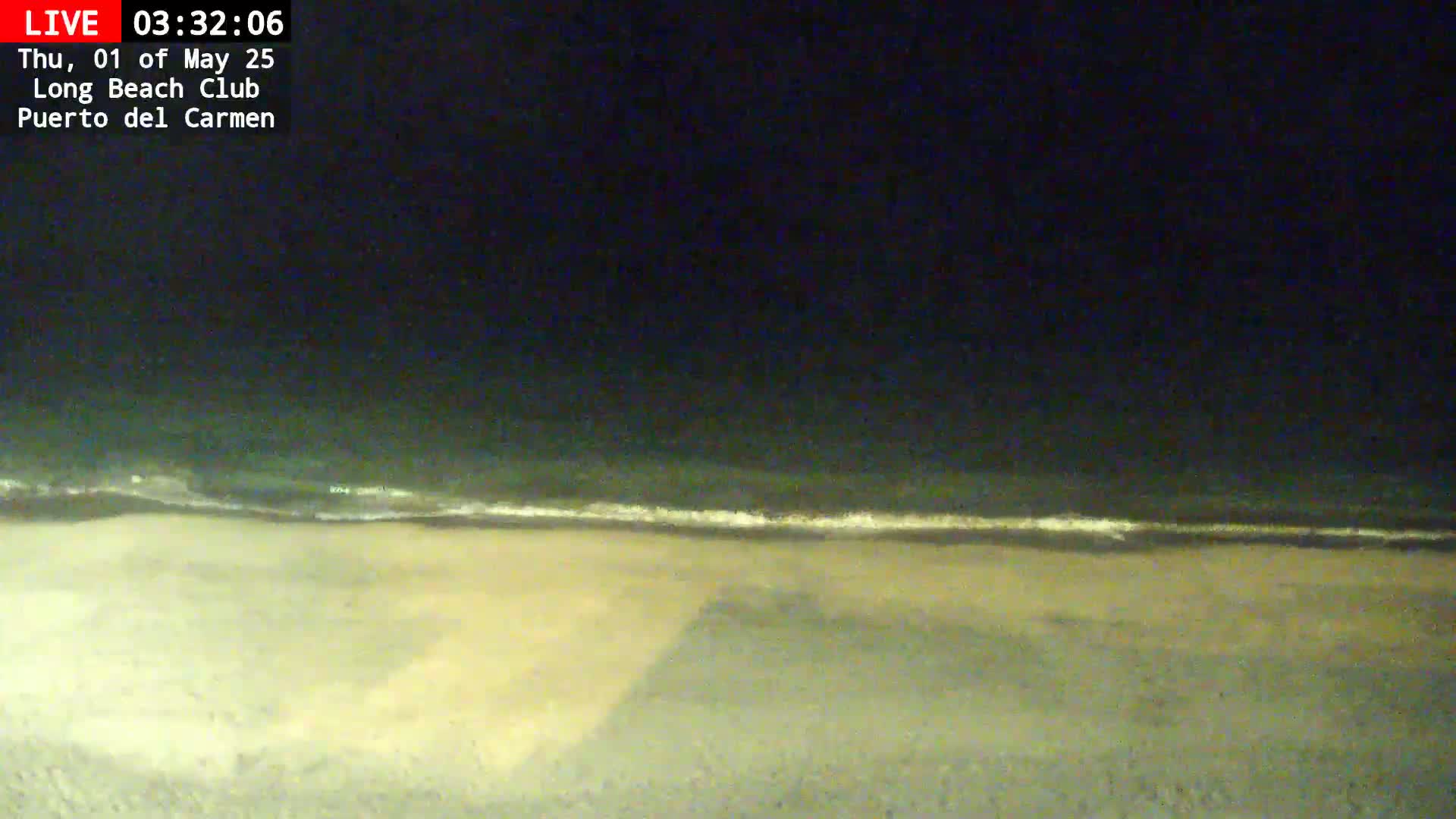 A dark, nighttime beach scene shows calm waves lapping a sandy shore under a clear, starless sky.