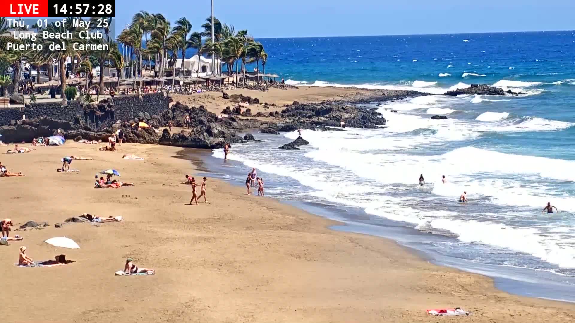 A sandy beach with people sunbathing and swimming in the ocean under sunny skies with a moderate breeze.