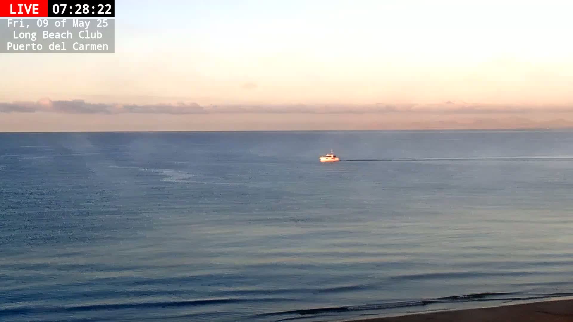 A small boat is visible on a calm ocean under a pale pink and orange sunrise sky with a few clouds.
