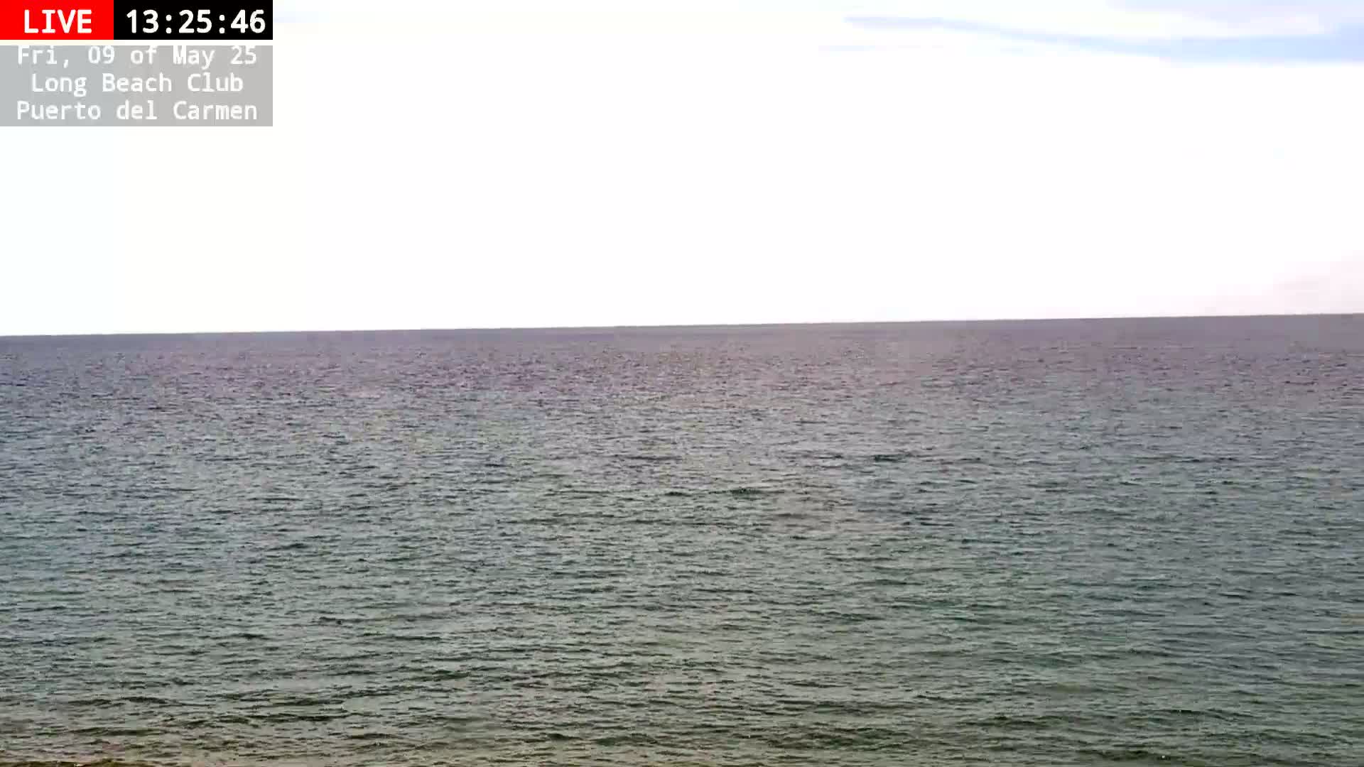 A mostly cloudy sky overlooks a calm, dark-green ocean.