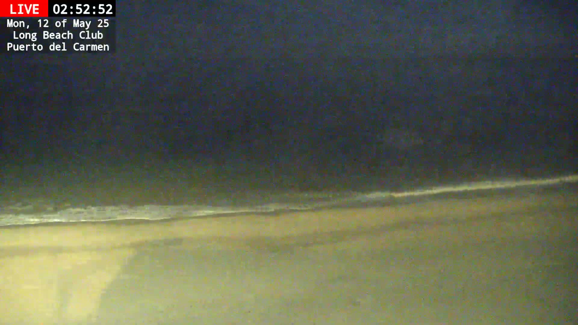 A dark, nighttime view shows a sandy beach with a gently lapping ocean.