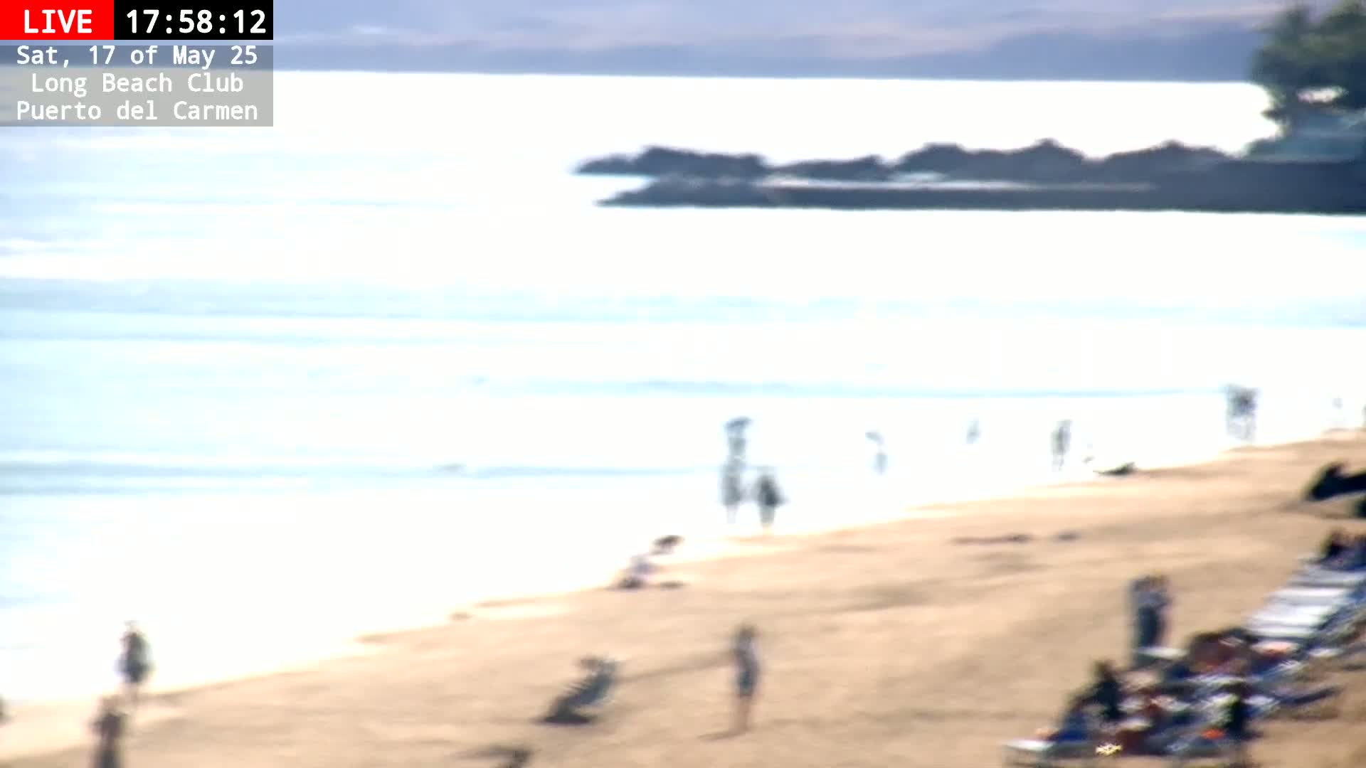 A long sandy beach with a calm ocean and several people scattered along the shore on a sunny day.