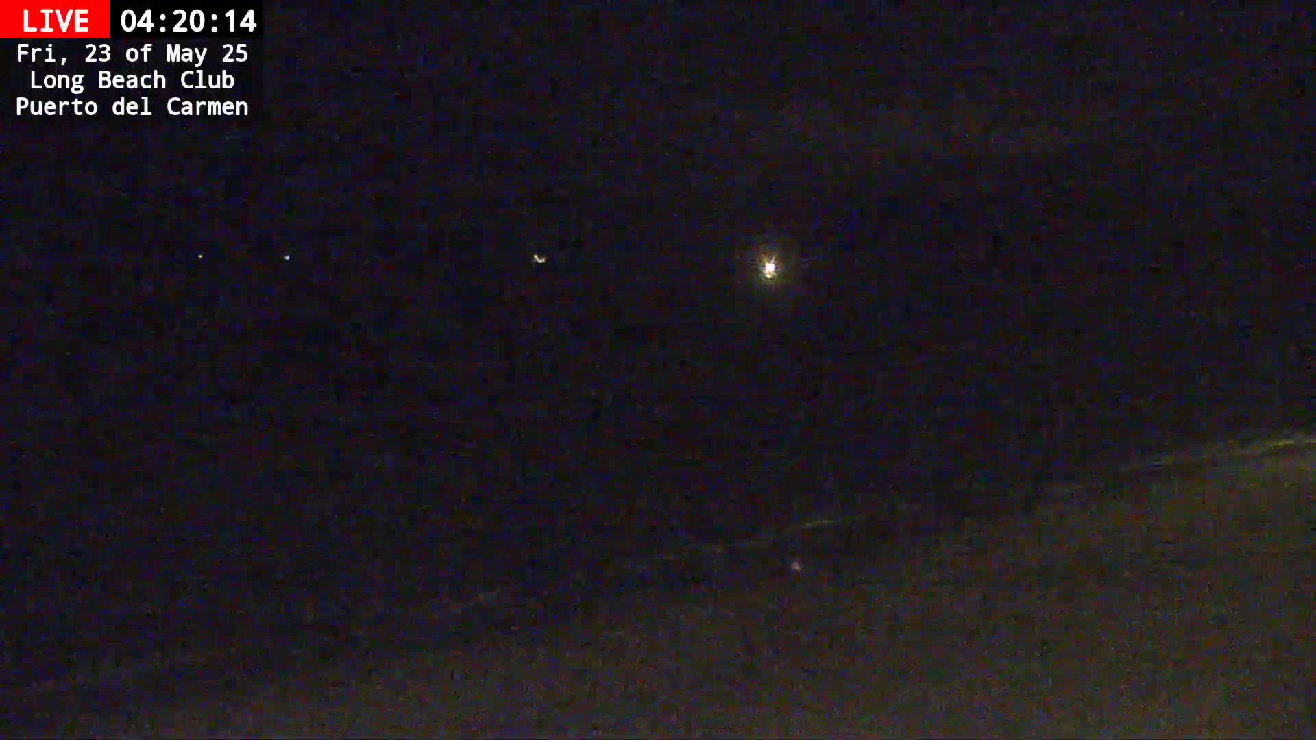 A nighttime, low-light view shows a dark landscape with a few faint lights in the distance under a clear, dark sky.
