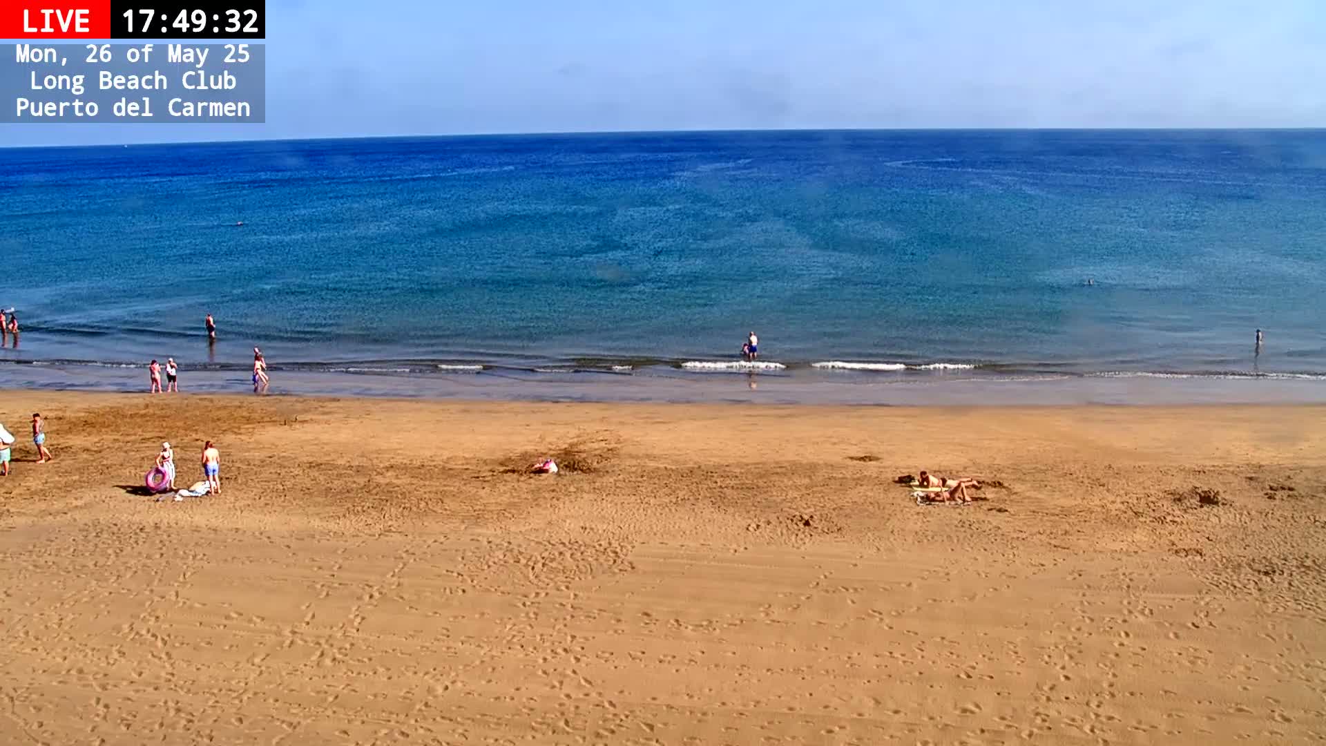 A sandy beach with a few people on it and a calm, blue ocean under a clear sky.