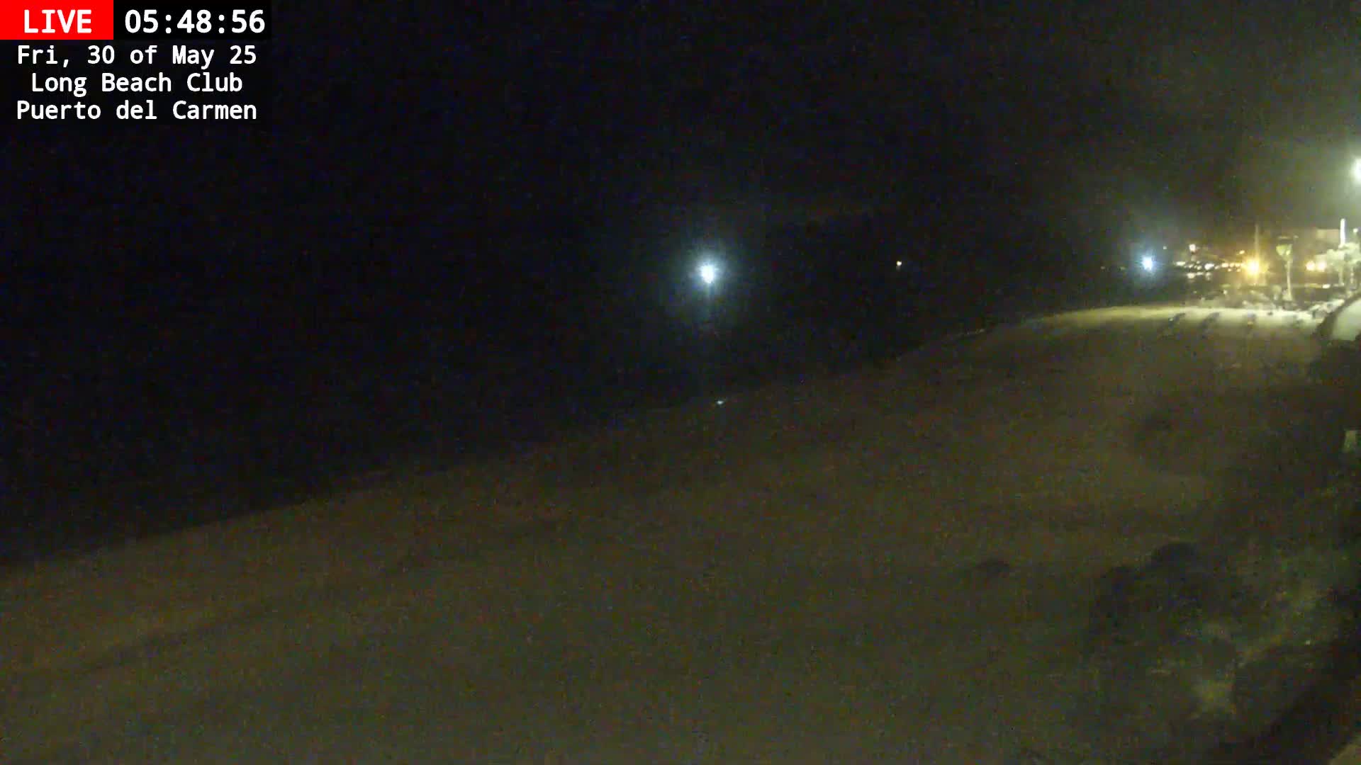A dark, nighttime beach scene is shown, with a few lights visible in the distance.