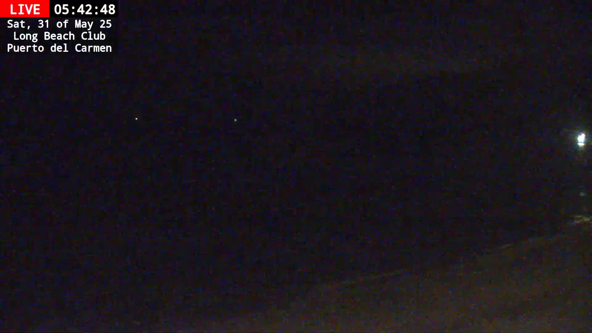 A dark nighttime scene shows a mostly clear sky with a few faint lights visible in the distance.