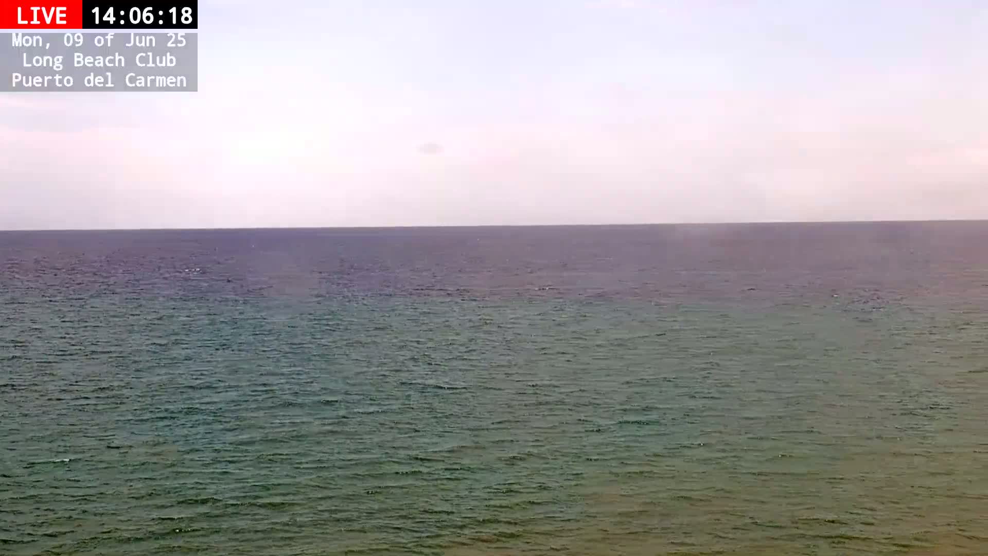 A mostly calm, greenish-blue ocean stretches to a pale, hazy horizon under a light overcast sky.