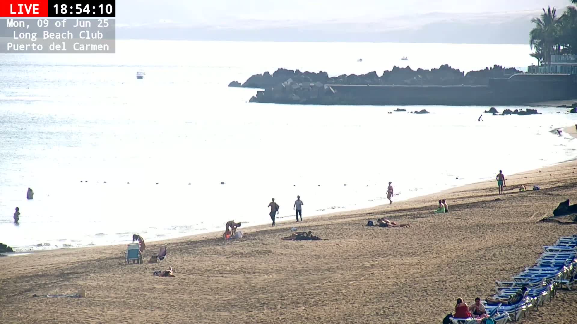 A sandy beach with a few people scattered on it and in the calm ocean water, under a hazy sky.