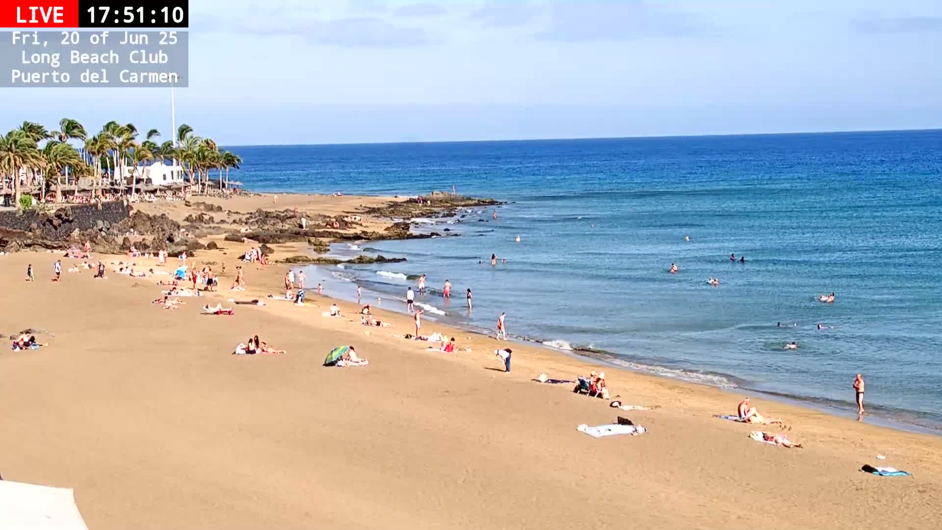 A sandy beach with many people sunbathing and swimming in a clear blue ocean under a sunny sky.