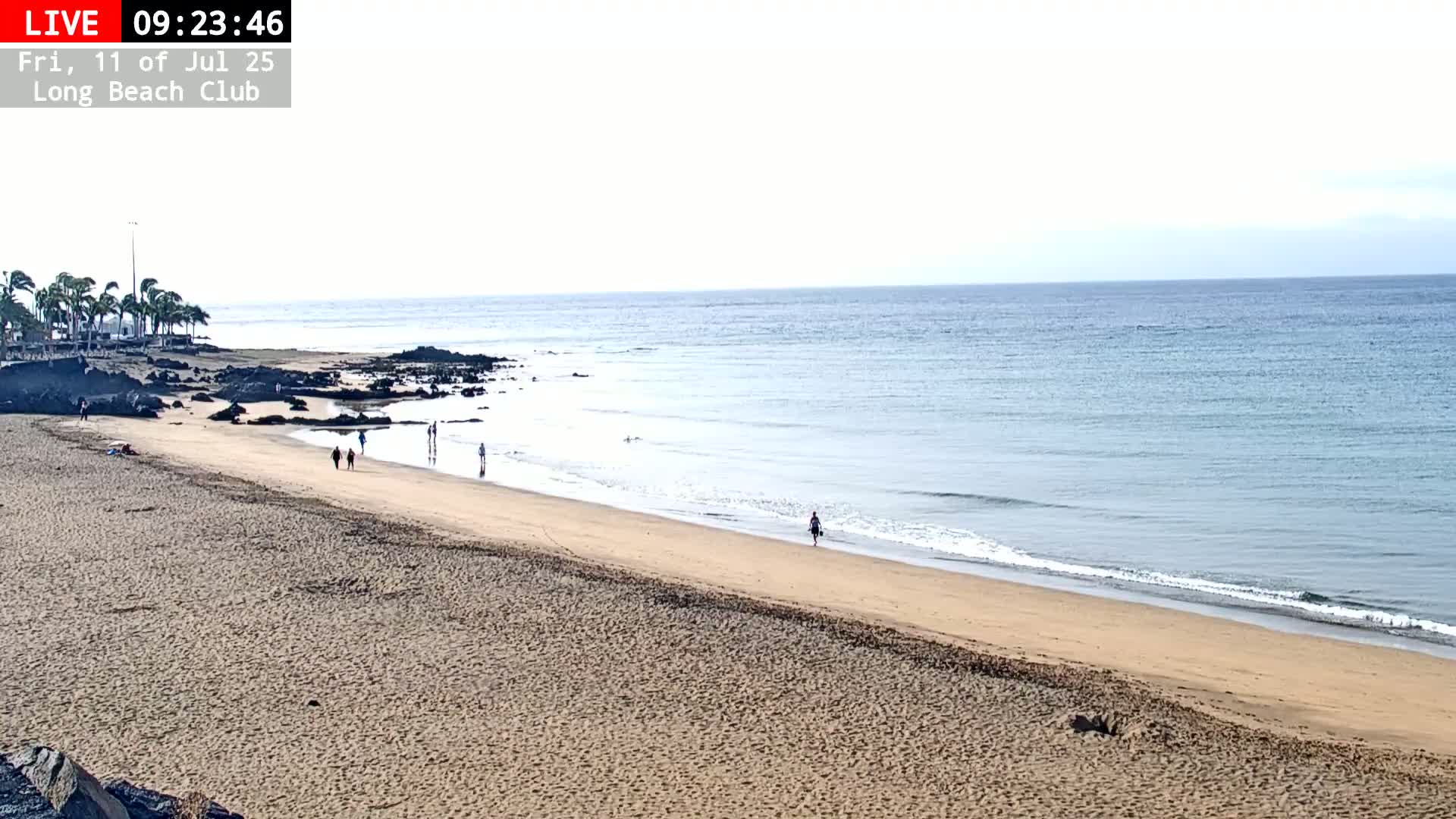 A mostly sunny beach with a calm ocean and several people walking along the shore.