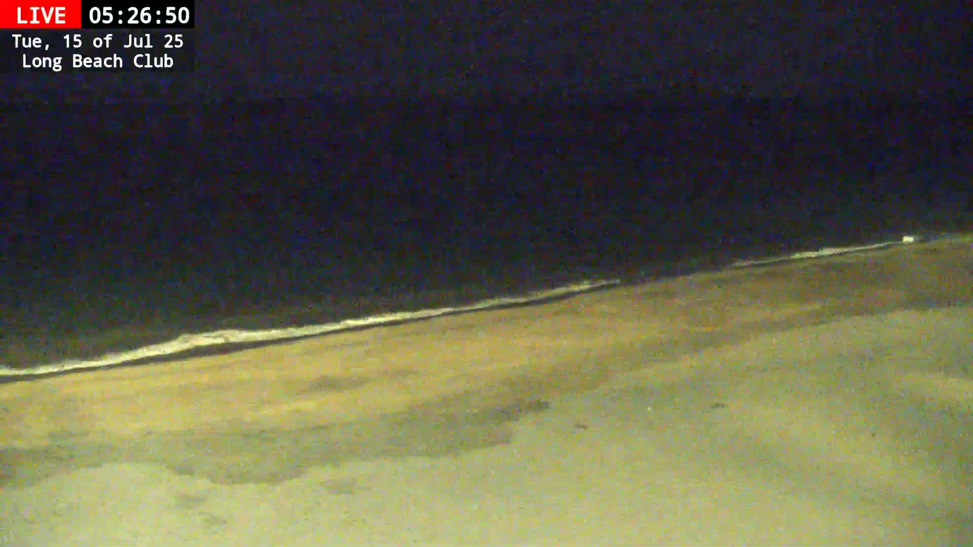 A dark beach at night shows a gently lapping ocean and a mostly empty sandy shore.
