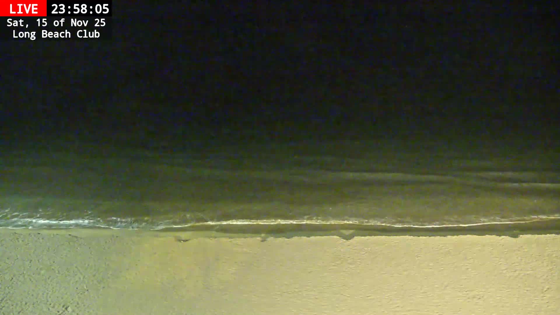 The image displays a clear night view of a beach, with dark ocean water featuring a line of white surf meeting the faintly illuminated sand.