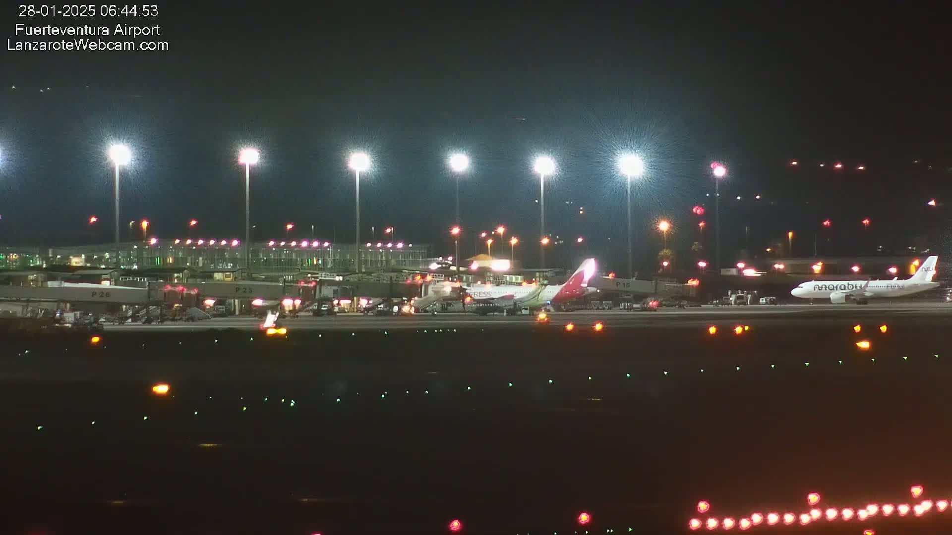 At night, several airplanes are parked at an airport terminal under bright lights.