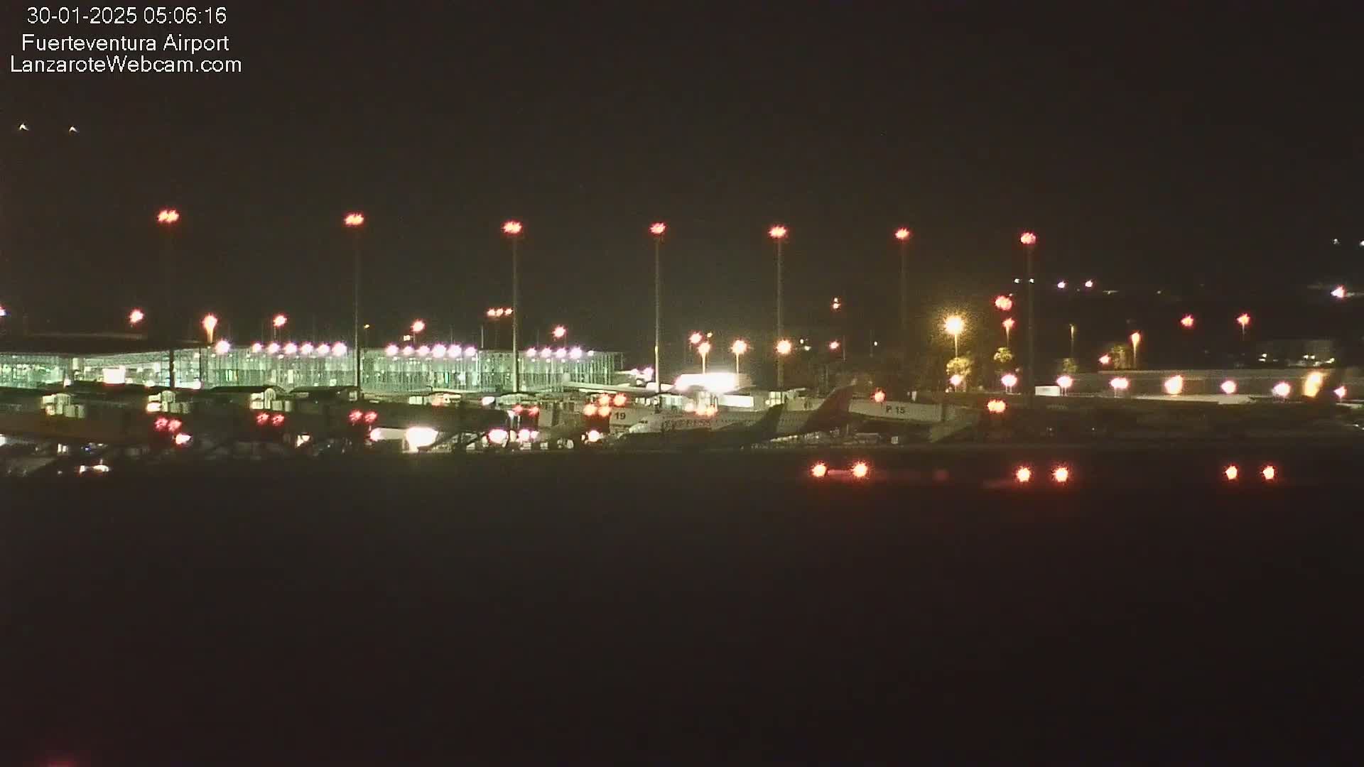 A nighttime view of an airport terminal and several airplanes on the tarmac, illuminated by bright lights under a clear, dark sky.