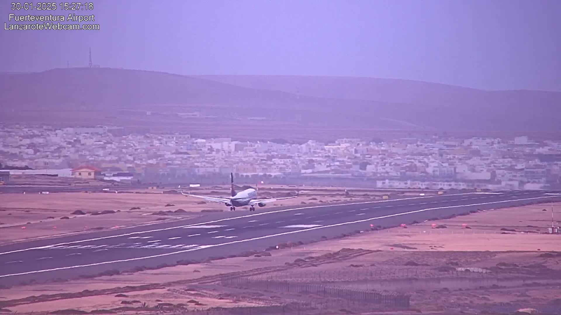 A passenger airplane is landing on a runway at an airport, with a hazy, muted-colored landscape in the background.