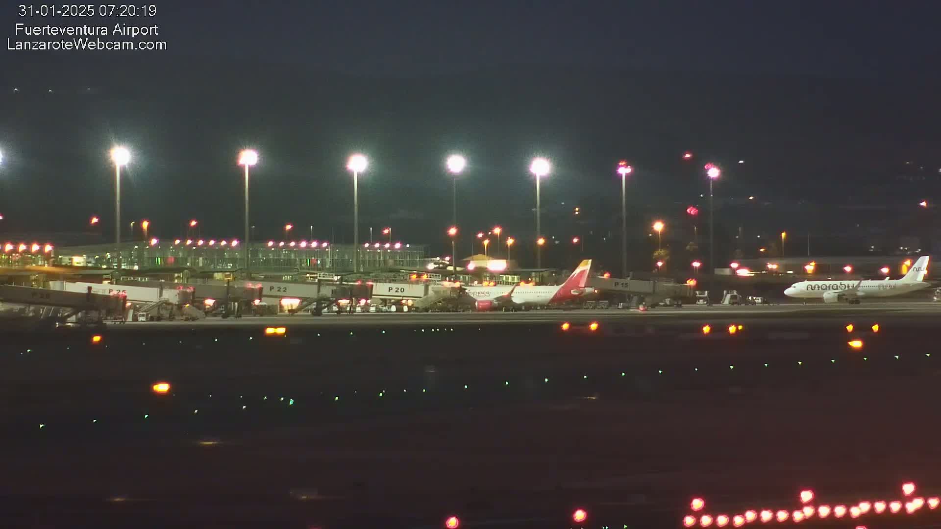 At night, two airplanes are parked at an airport terminal under bright lights.
